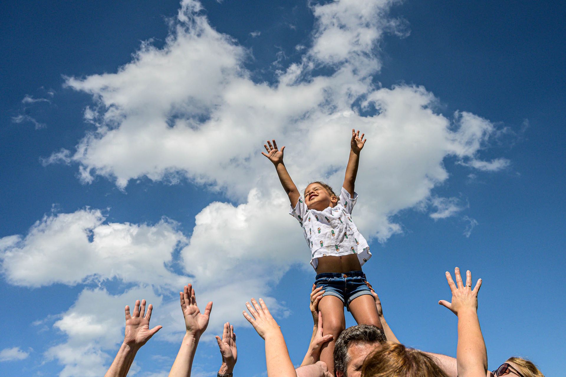 Een groep mensen houdt een klein meisje in de lucht.