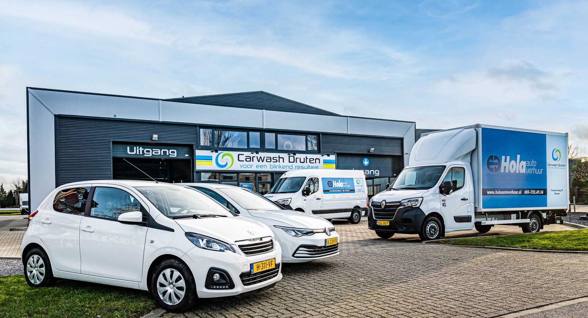 Een rij witte auto's en busjes geparkeerd voor een gebouw.