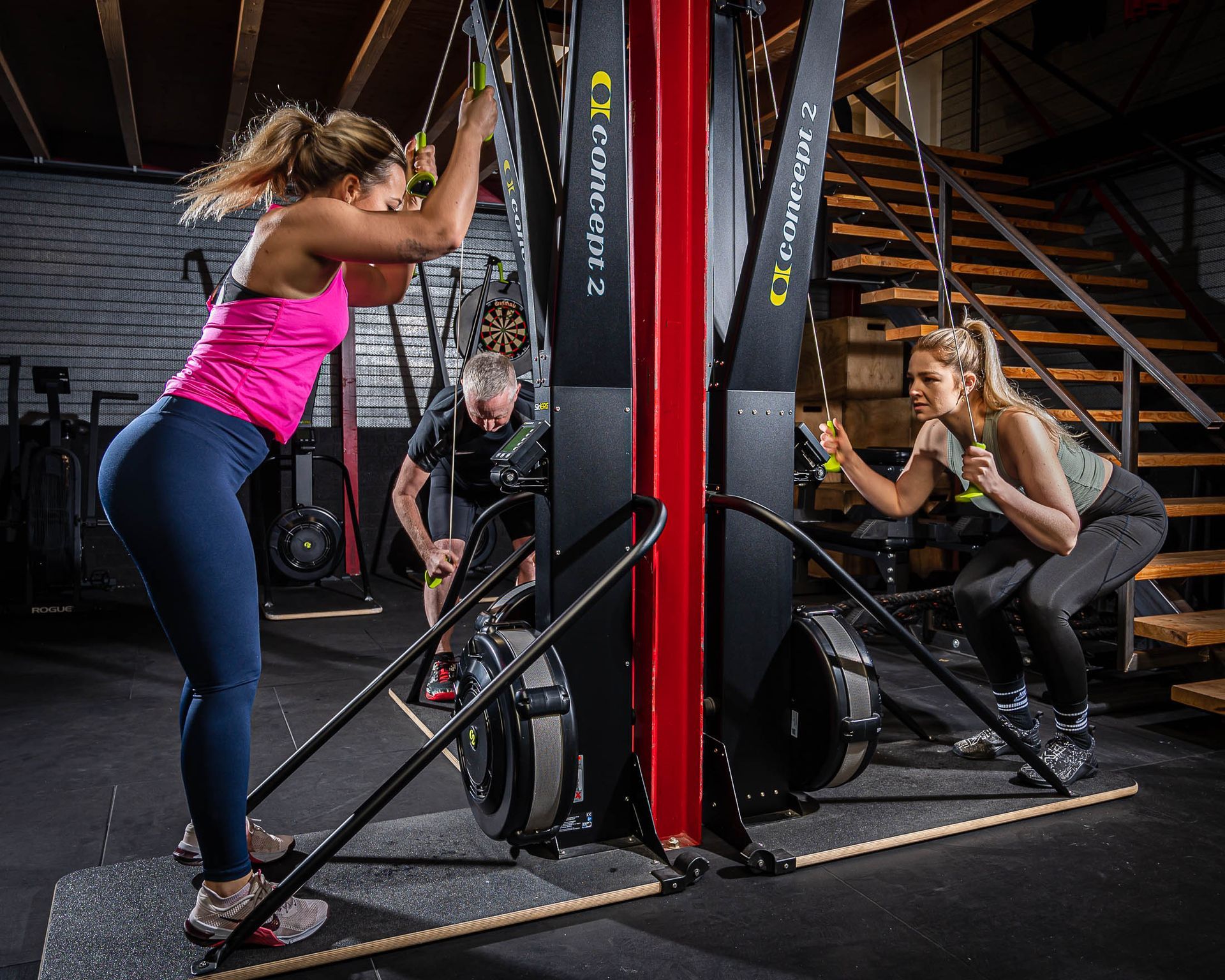Een vrouw in een roze shirt hurkt op een machine in een sportschool