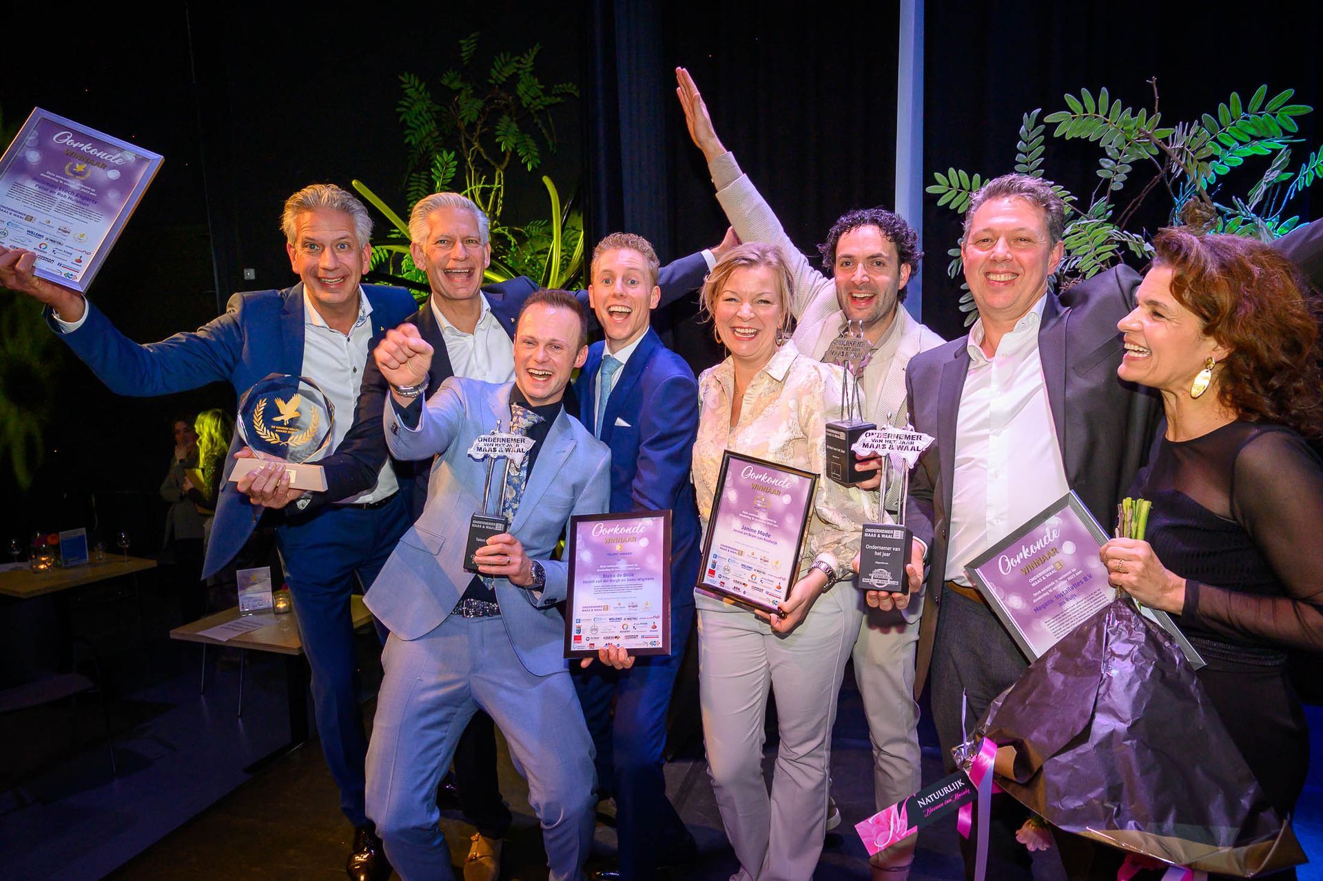 Een groep mensen poseert voor een foto terwijl ze trofeeën vasthouden.