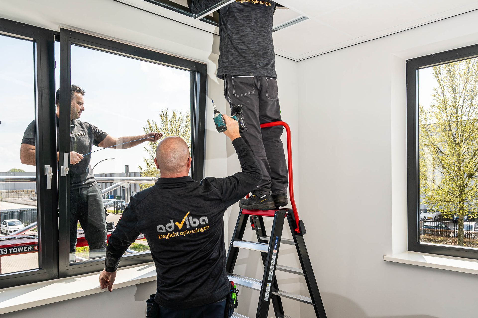 Een man staat op een ladder en werkt aan een raam.