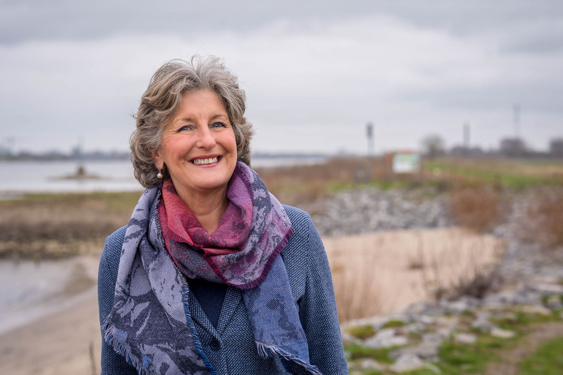 Een vrouw die een sjaal en een blauw jasje draagt, lacht.