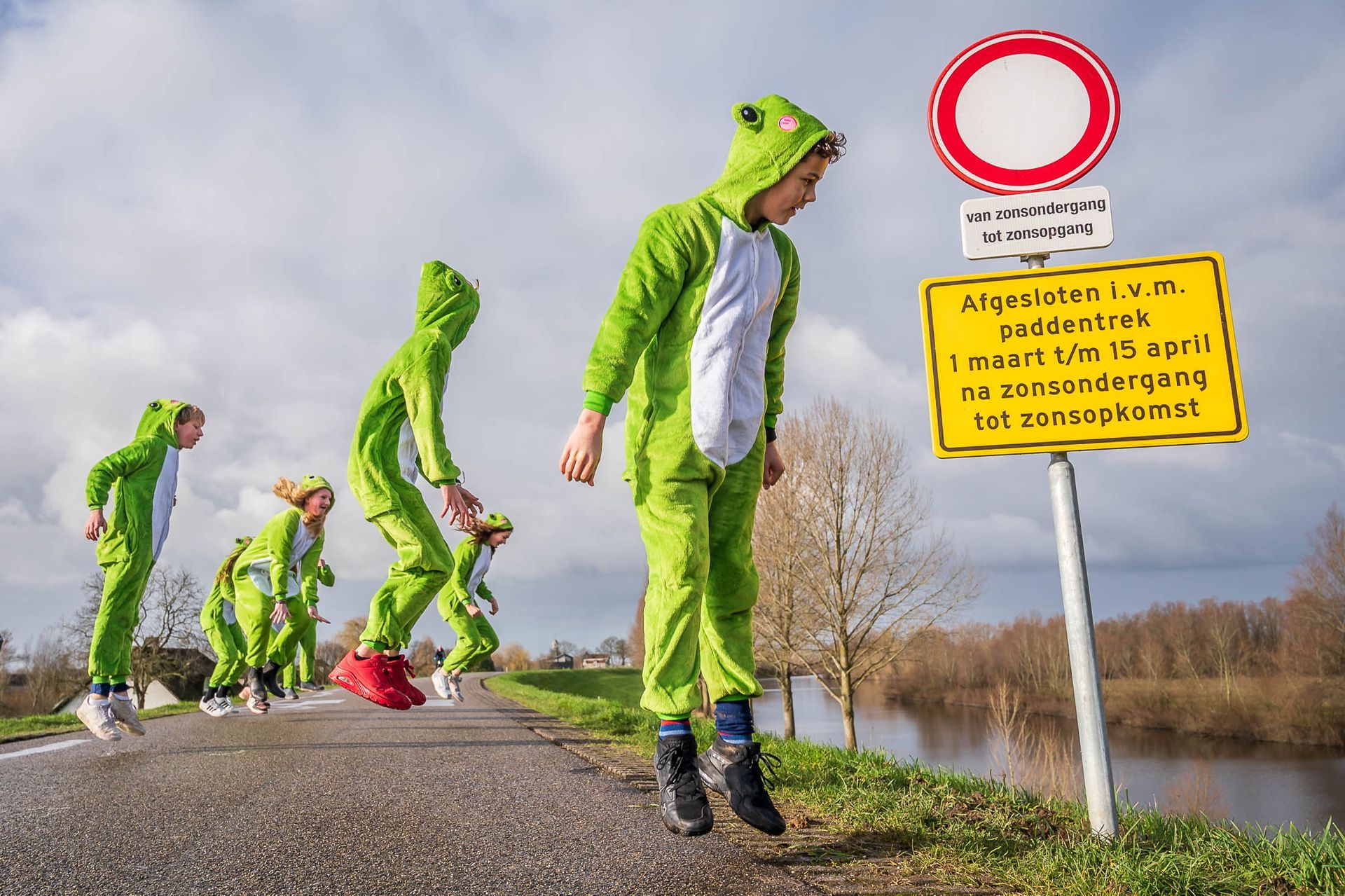 Een groep mensen gekleed in groene kikkerkostuums loopt over een weg.