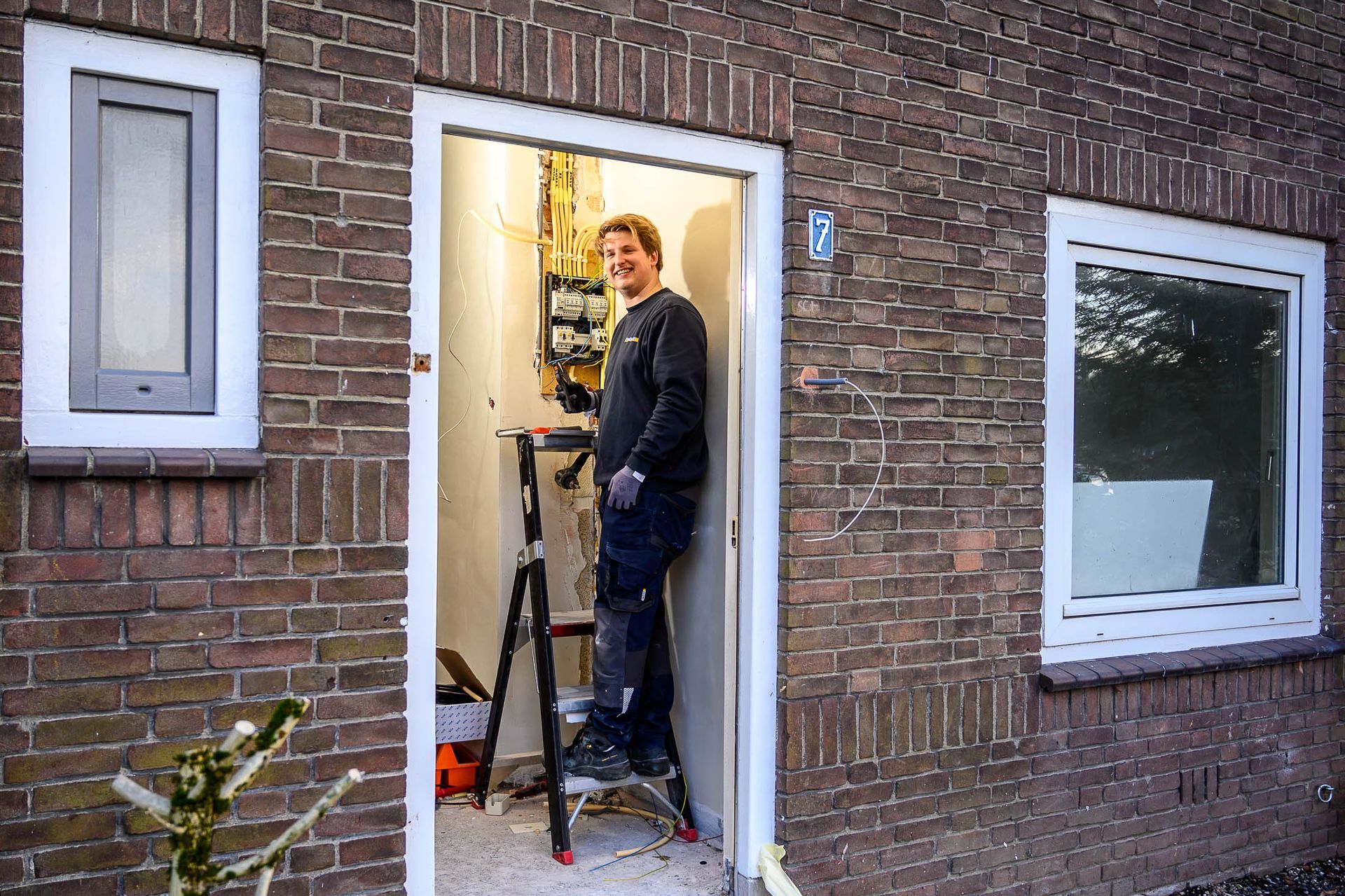 Een man staat in de deuropening van een bakstenen gebouw met een ladder.