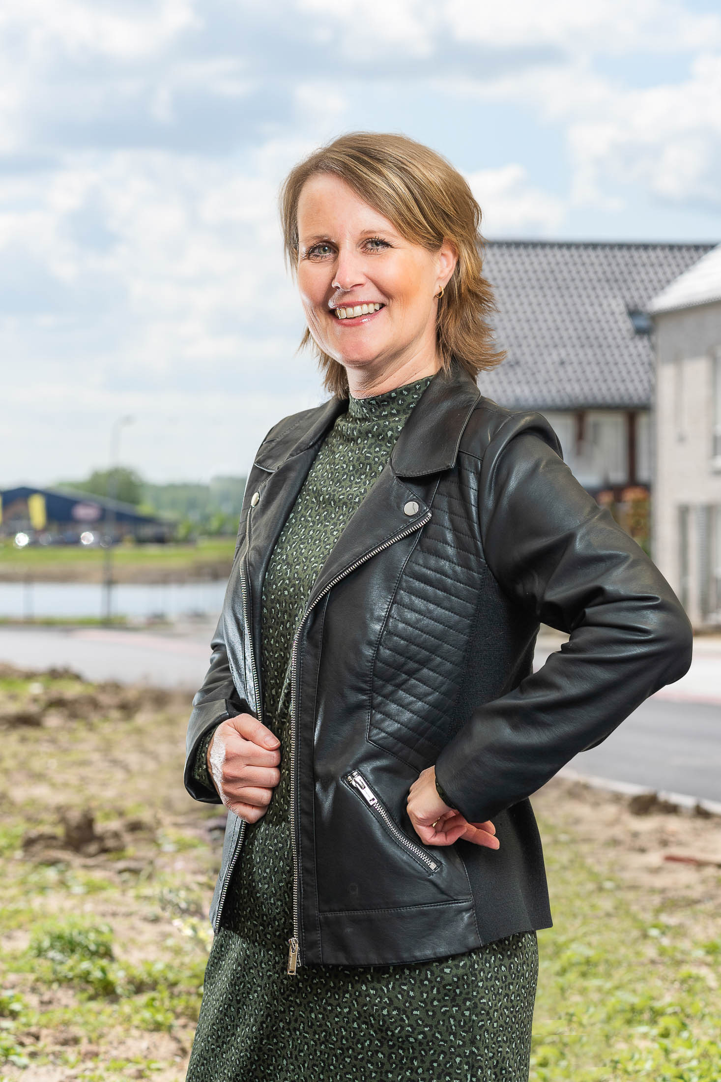 Een vrouw in een zwart leren jasje en een groene jurk staat in een veld.