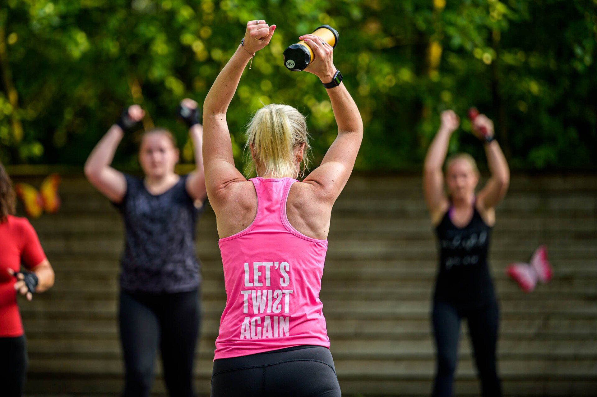 Een vrouw in een roze tanktop leert een groep vrouwen hoe ze oefeningen moeten doen.