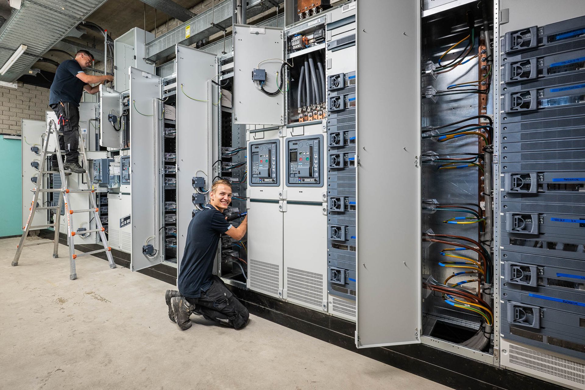 Twee mannen werken in een kamer aan elektrische apparatuur.