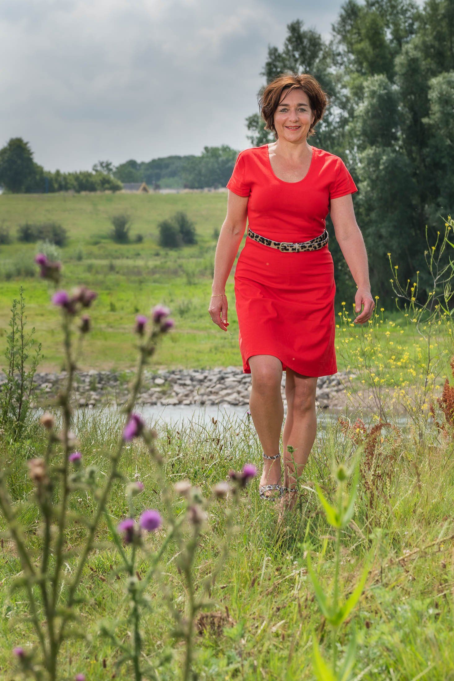 Een vrouw in een rode jurk loopt door een veld.