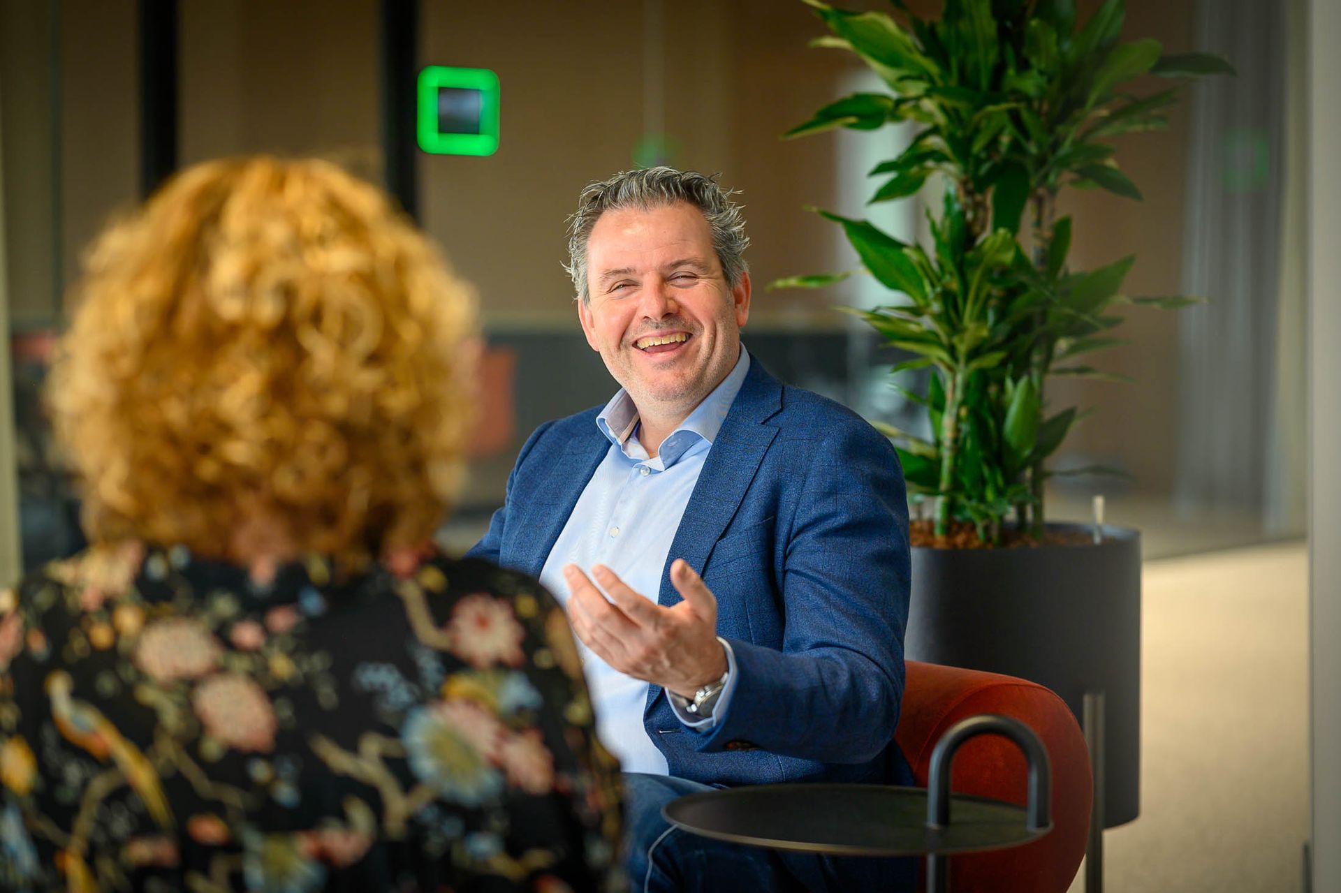 Een man in pak zit op een stoel en praat met een vrouw.