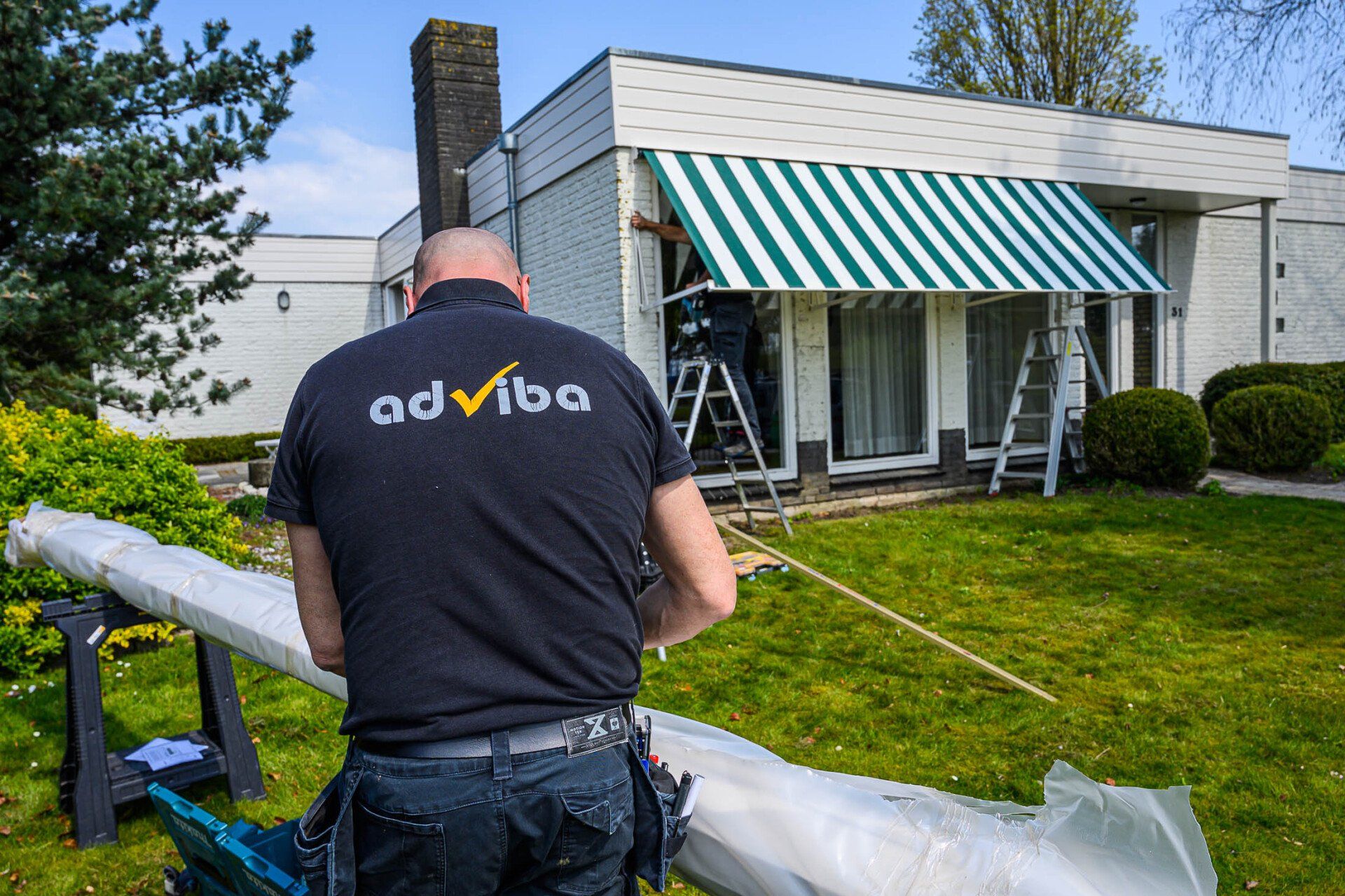 Een man staat voor een huis met een groen-witte luifel.