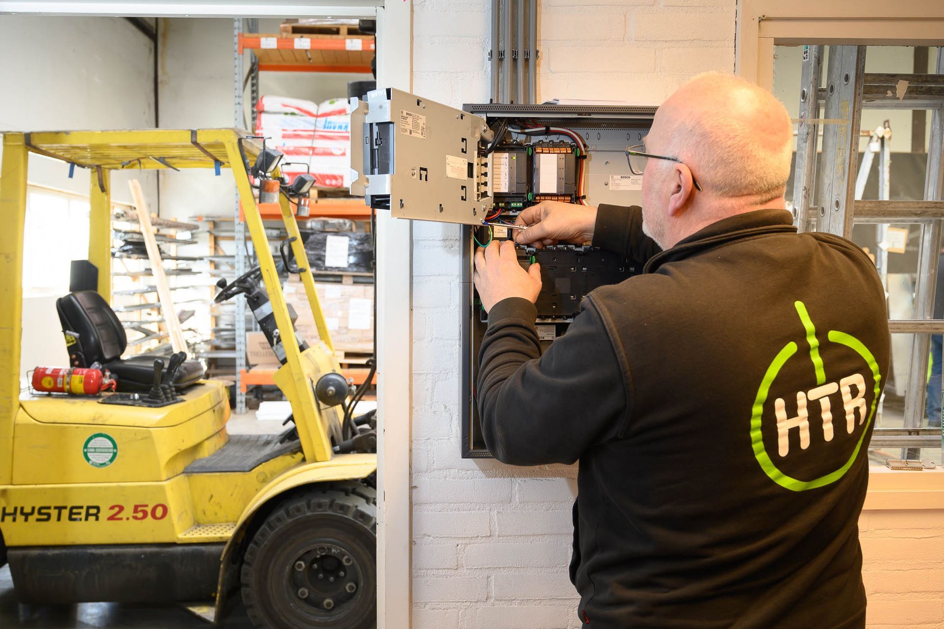 Een man werkt aan een elektrische kast naast een vorkheftruck.
