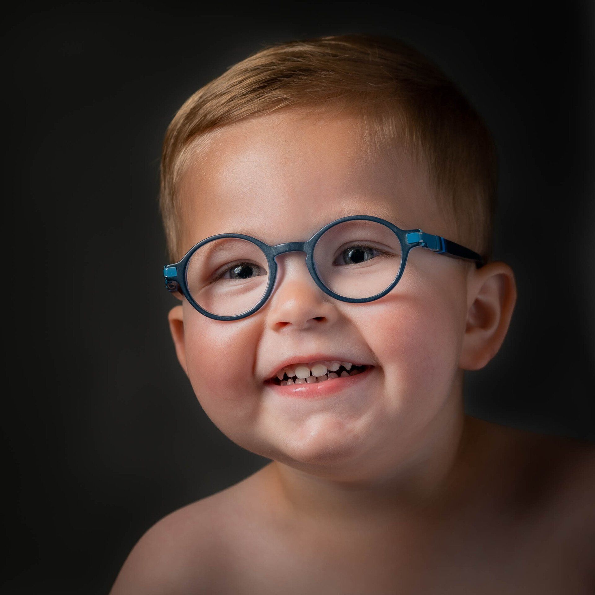 Een jonge jongen met een bril lacht naar de camera.