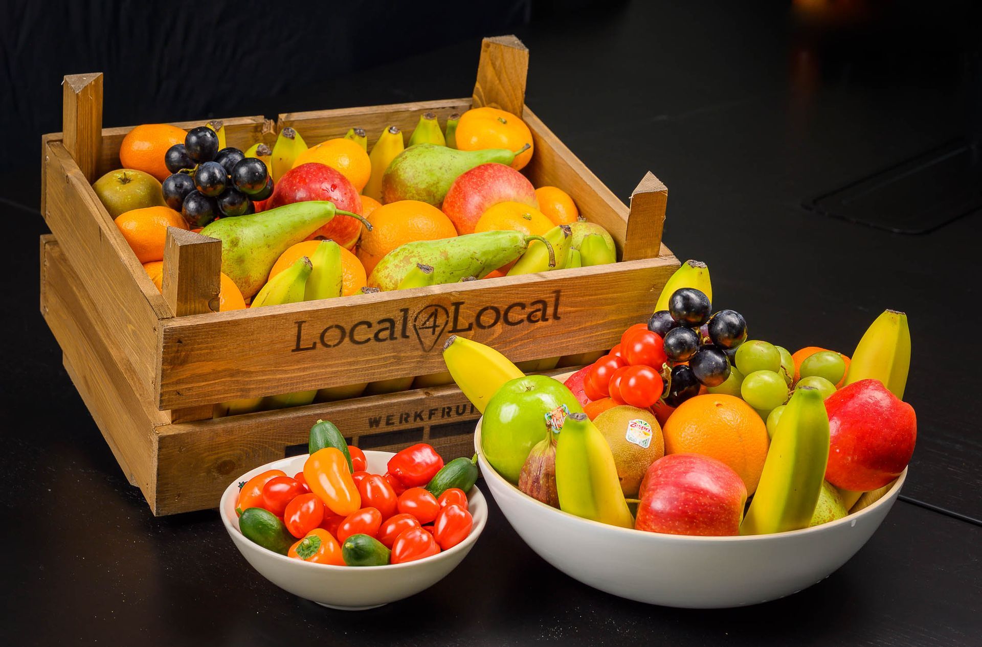 Een houten doos gevuld met fruit naast een schaal met fruit