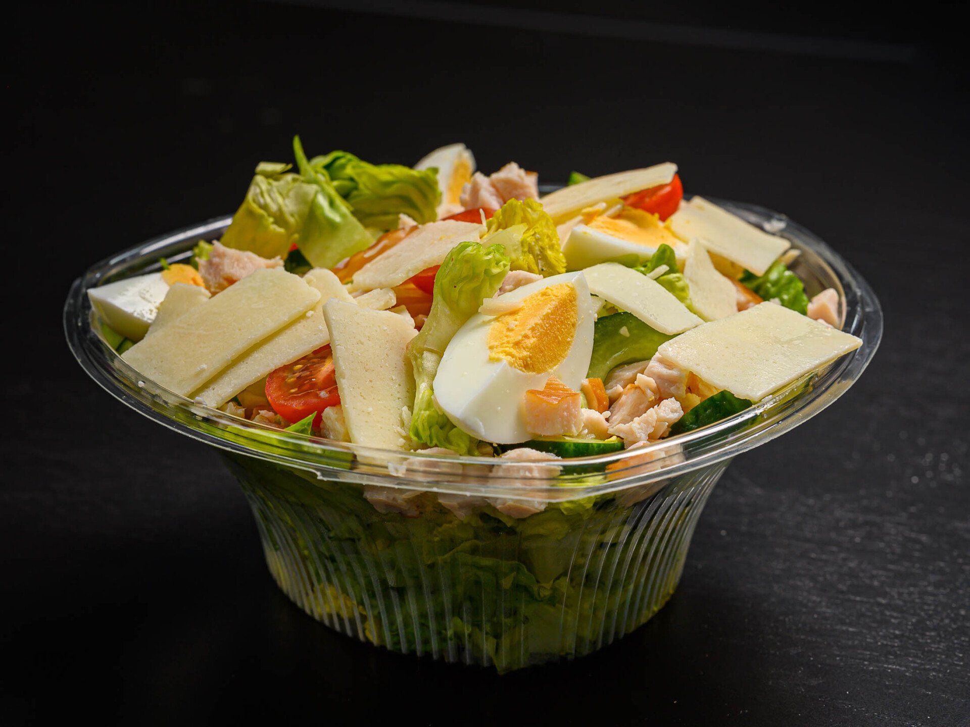 Een close-up van een salade in een plastic bakje op een tafel.
