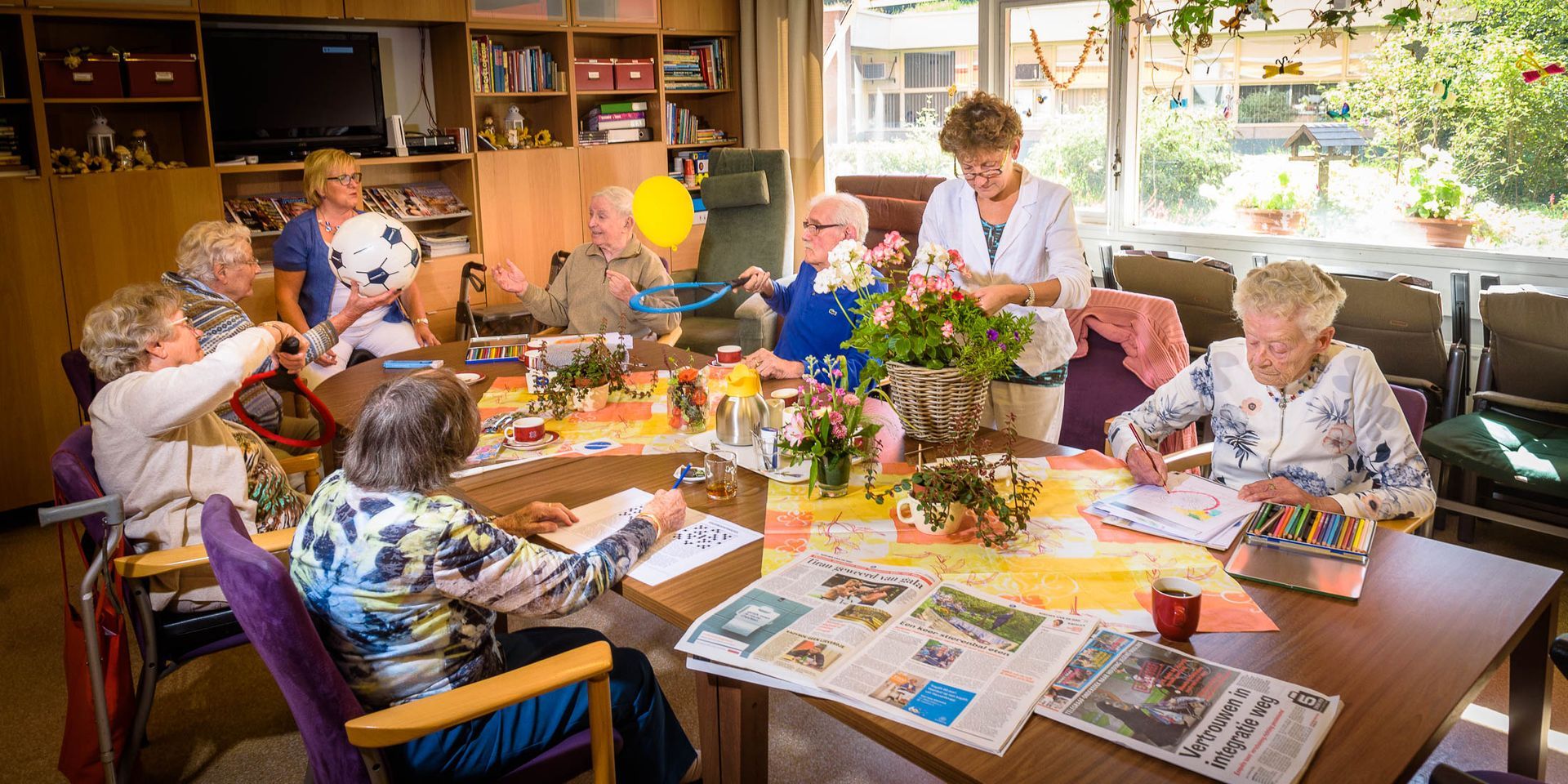 Een groep ouderen zit rond een tafel in een verzorgingshuis.