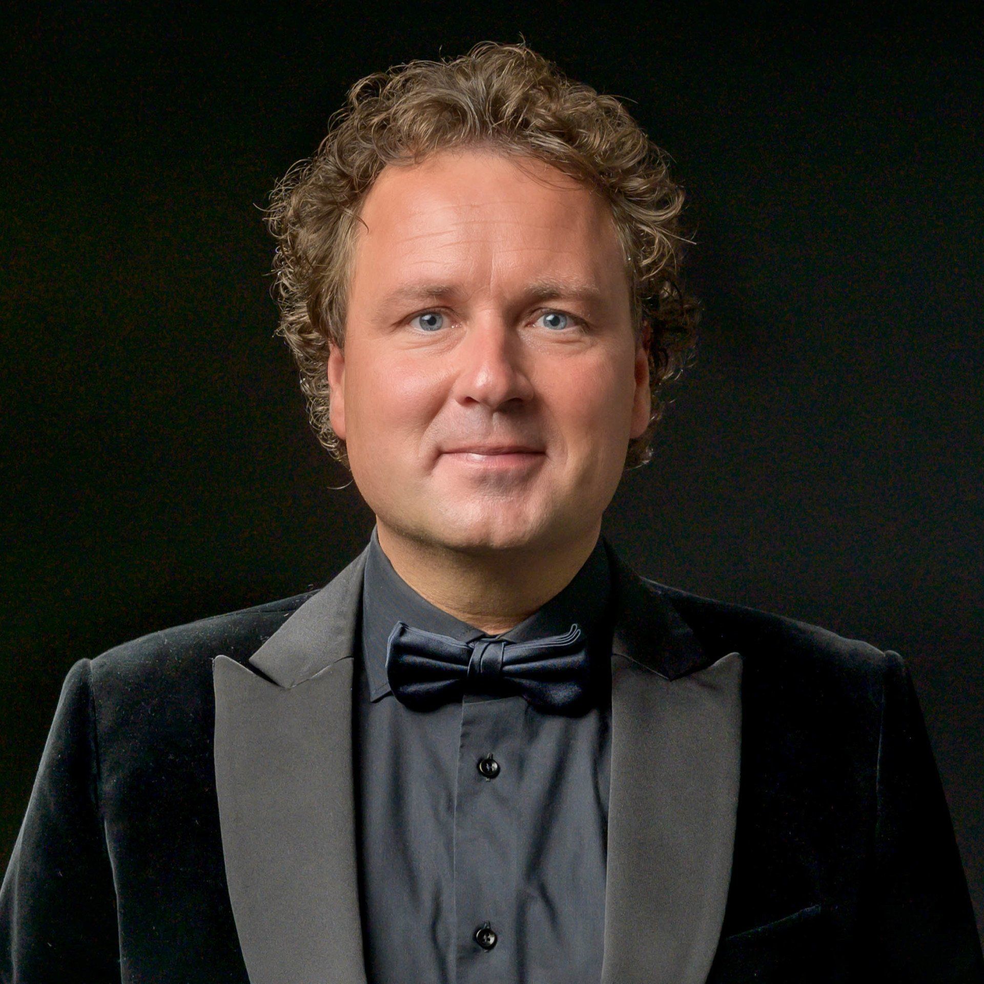 Een man met krullend haar draagt een smoking en een vlinderdas