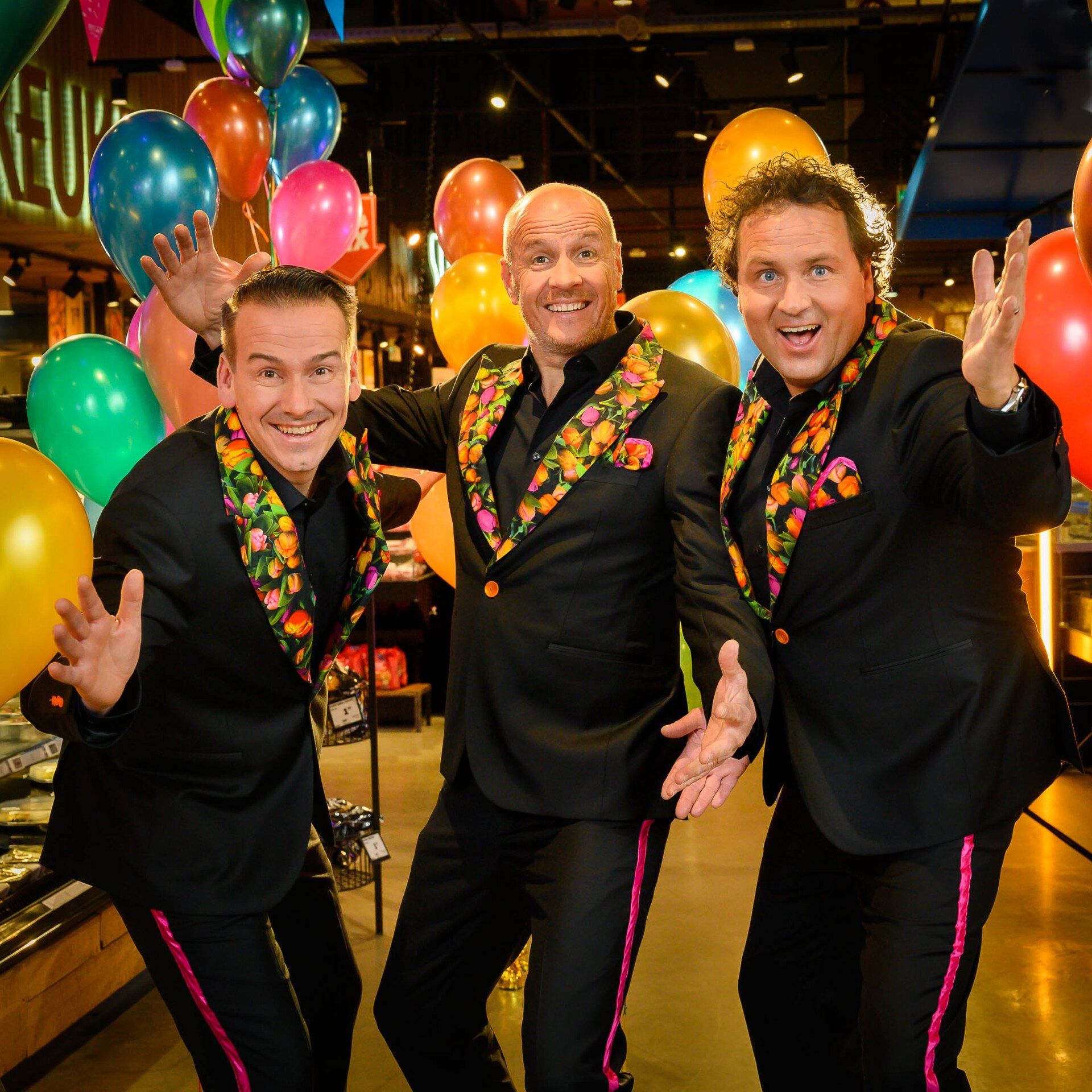 Drie mannen in pakken poseren voor een foto met ballonnen op de achtergrond
