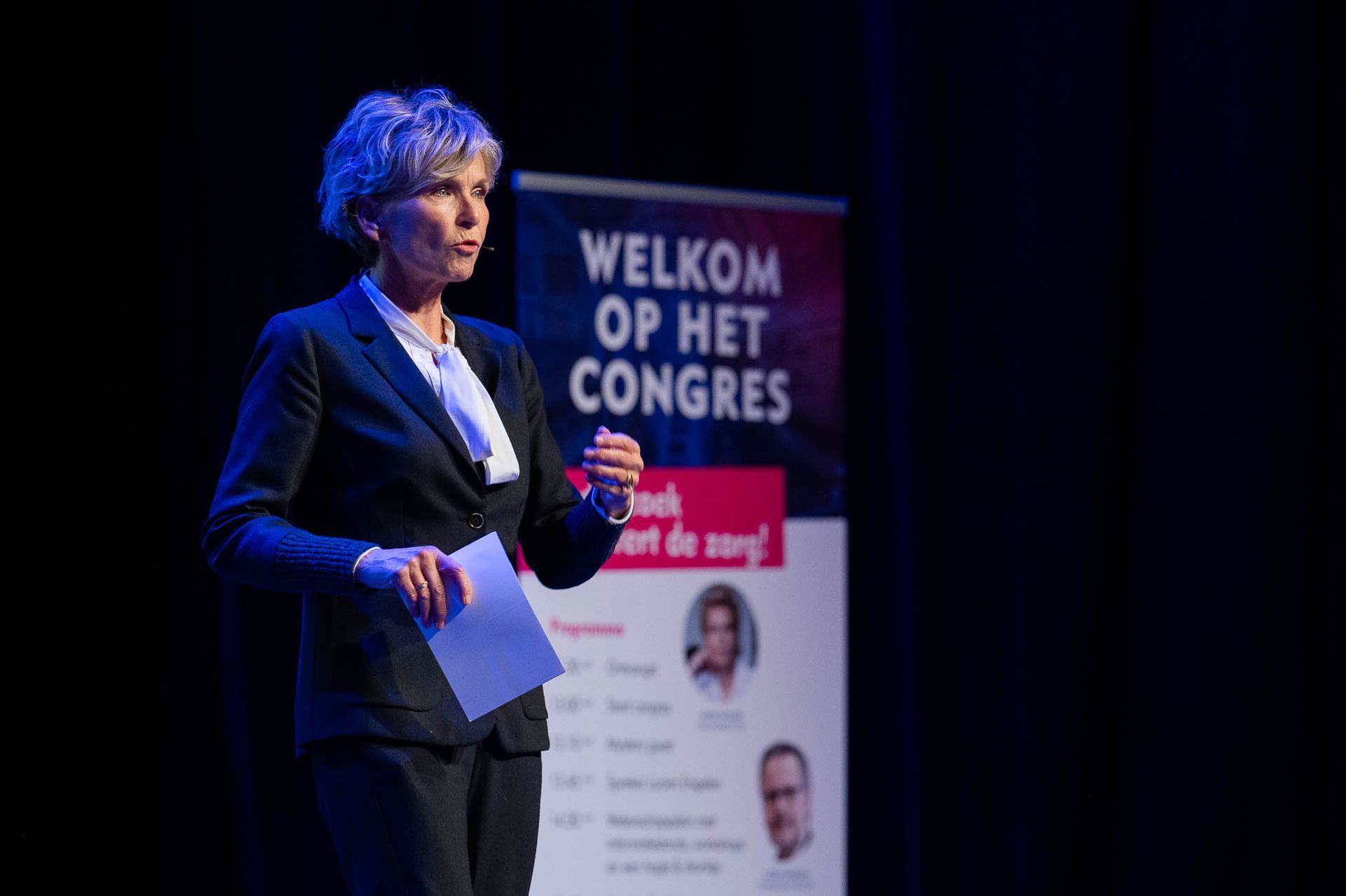 Een vrouw houdt een toespraak op een podium voor een bord met de tekst welkom op het congres.