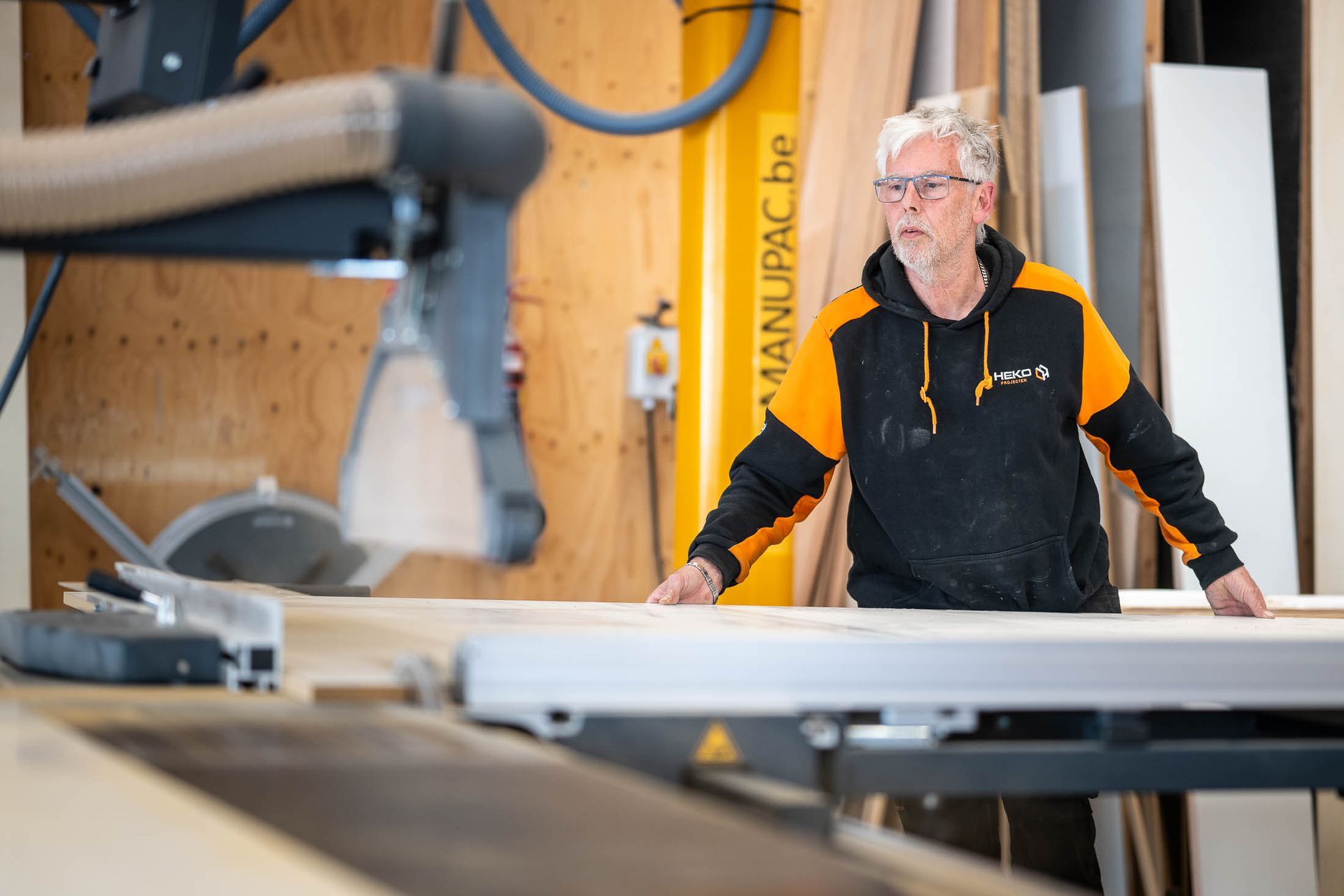 Een man staat voor een tafelzaag in een werkplaats.