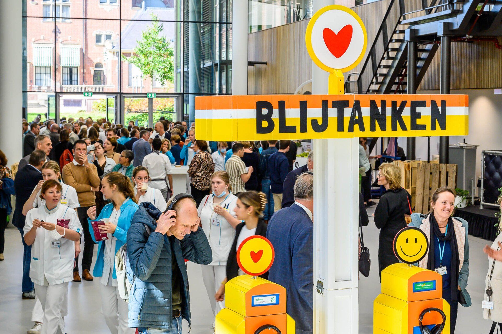 Een grote groep mensen staat onder een bord waarop 'blijtanken' staat.