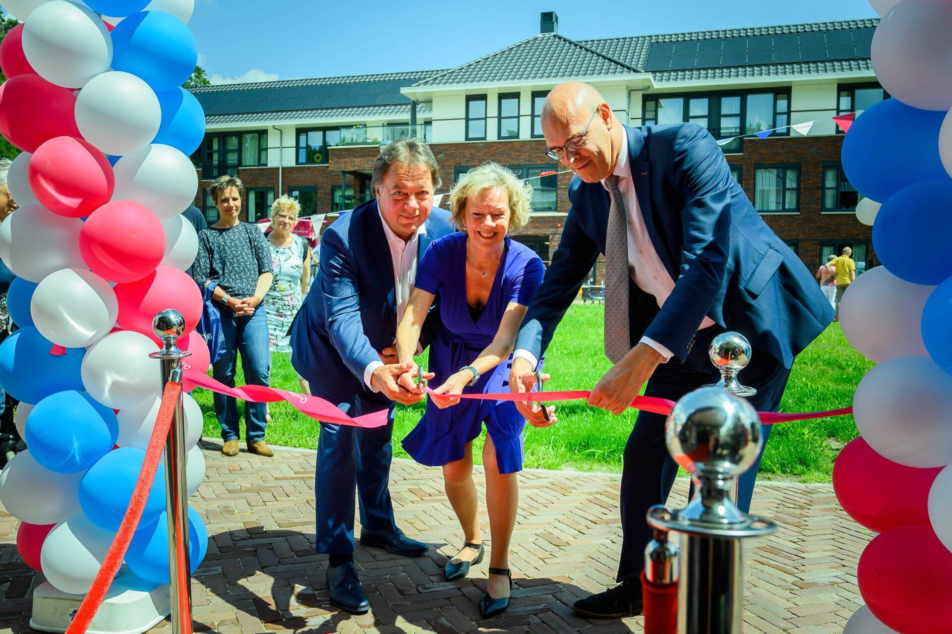 Drie mensen knippen een rood lint door voor een aantal ballonnen.