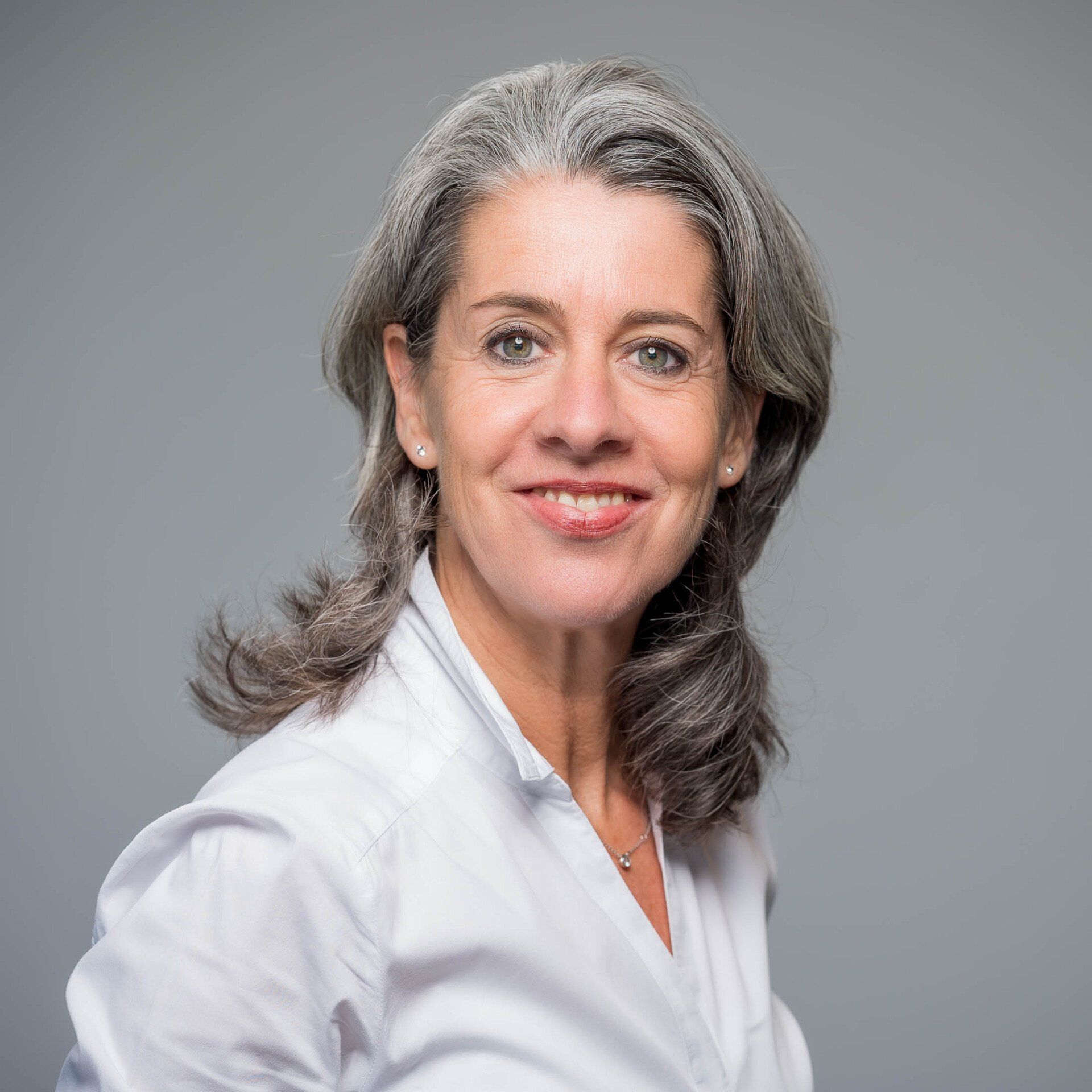 Een vrouw met grijs haar en een wit shirt lacht naar de camera.