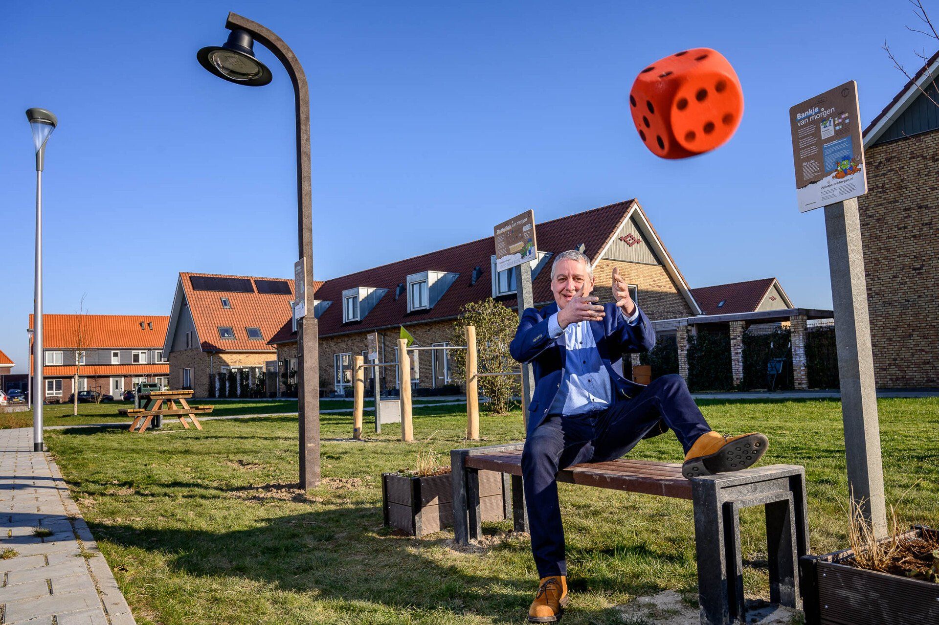 Een man zit op een bankje met een grote dobbelsteen in de lucht.