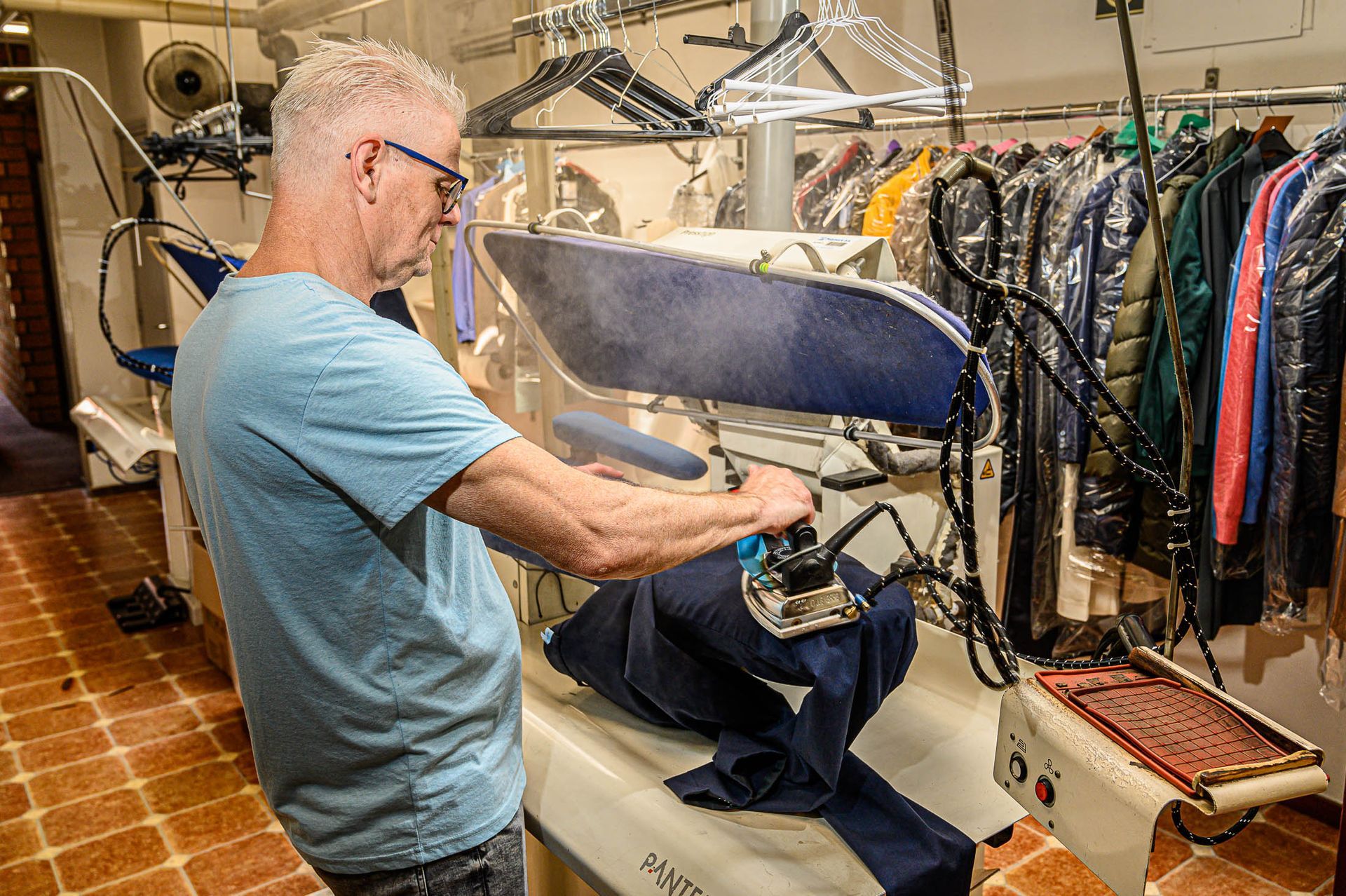 Een man strijkt een overhemd in een stomerij.
