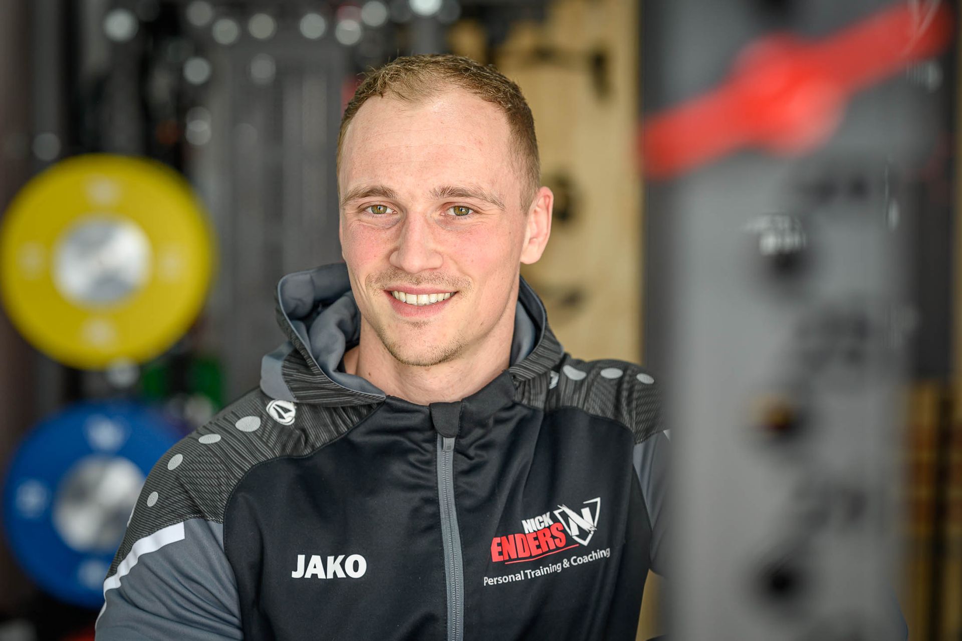 Een man in een hoodie lacht naar de camera in een sportschool.