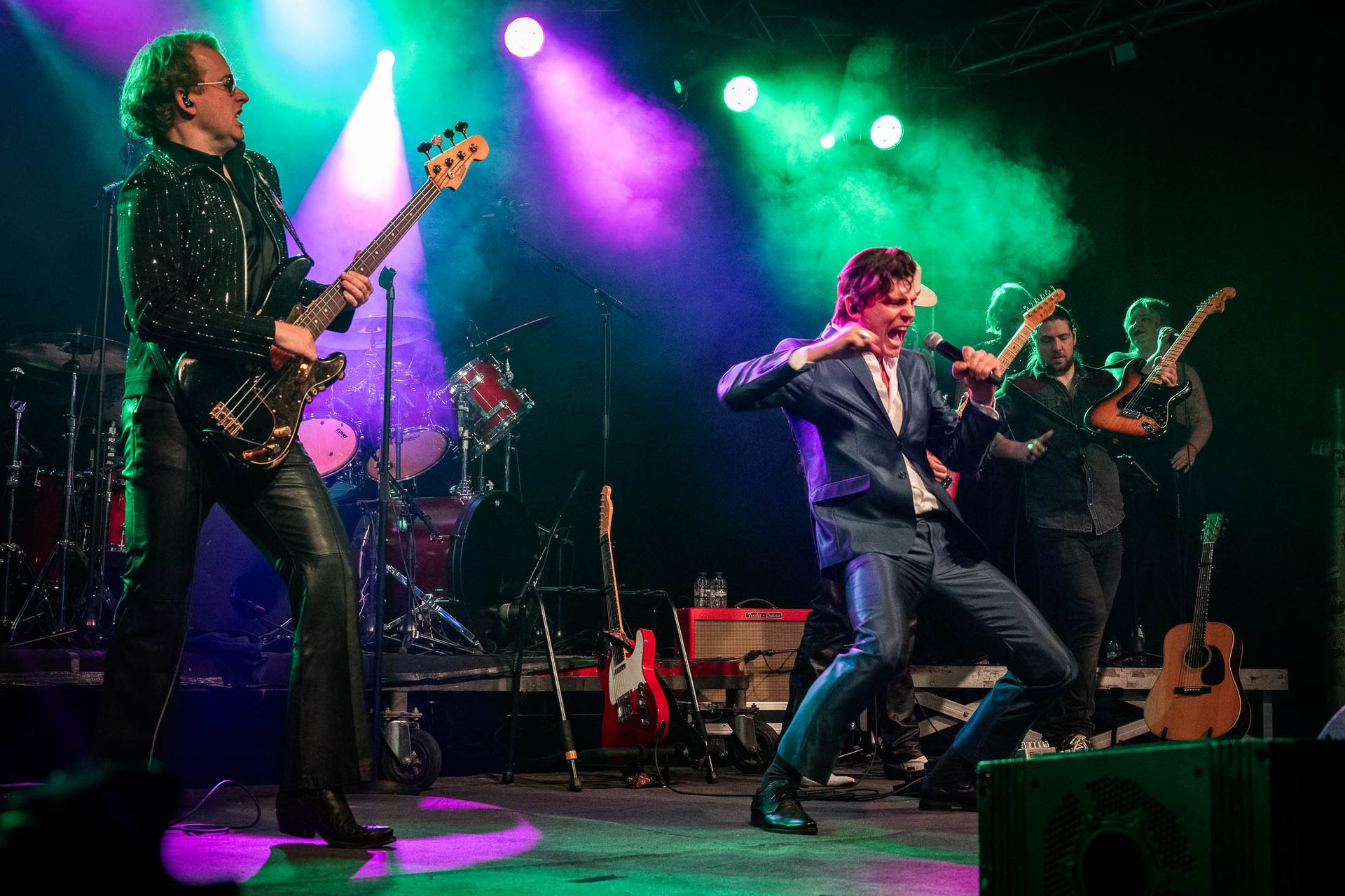 Een groep mannen speelt gitaar en zingt op een podium.