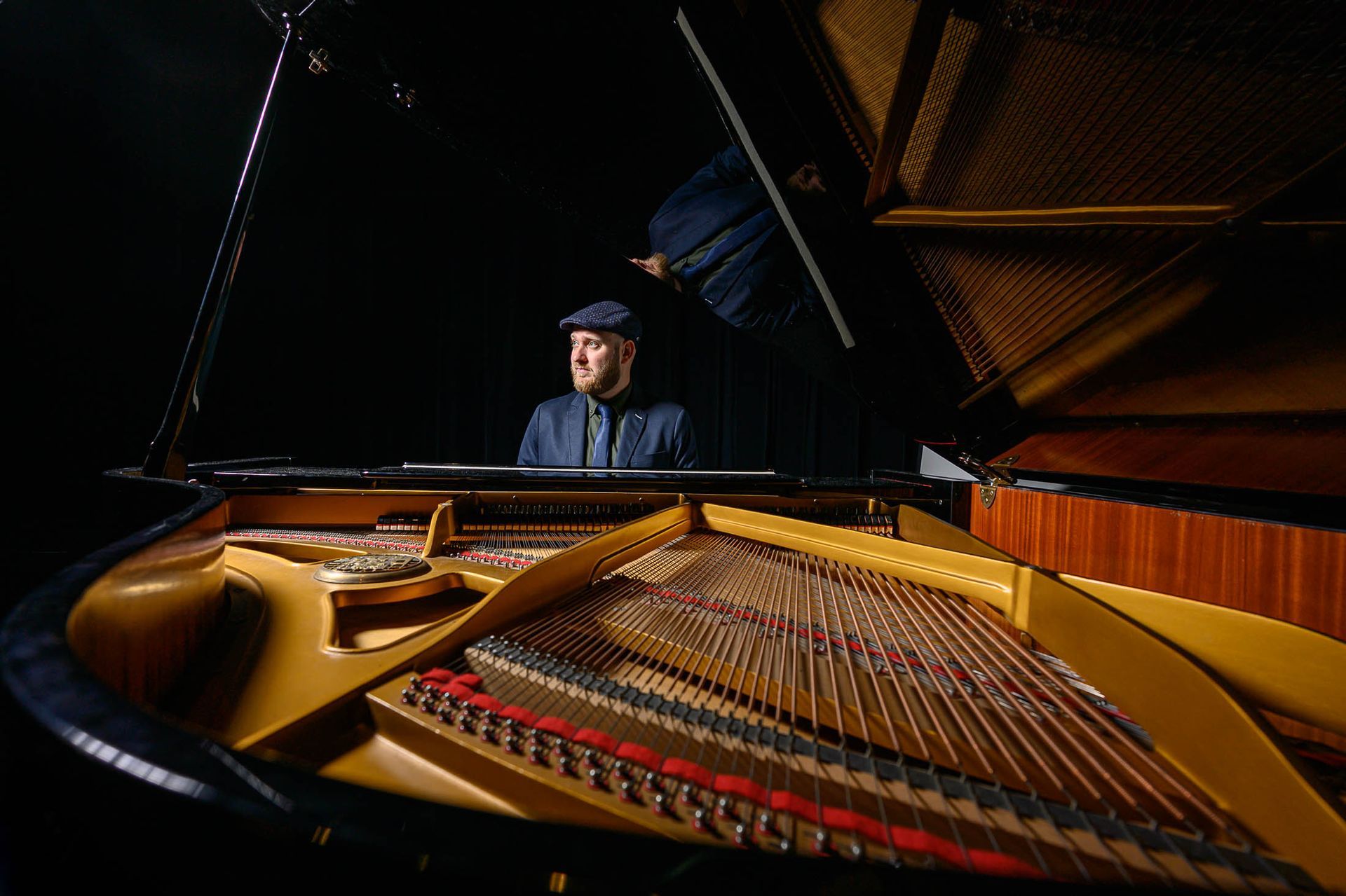 Een man zit achter een piano in een donkere kamer.