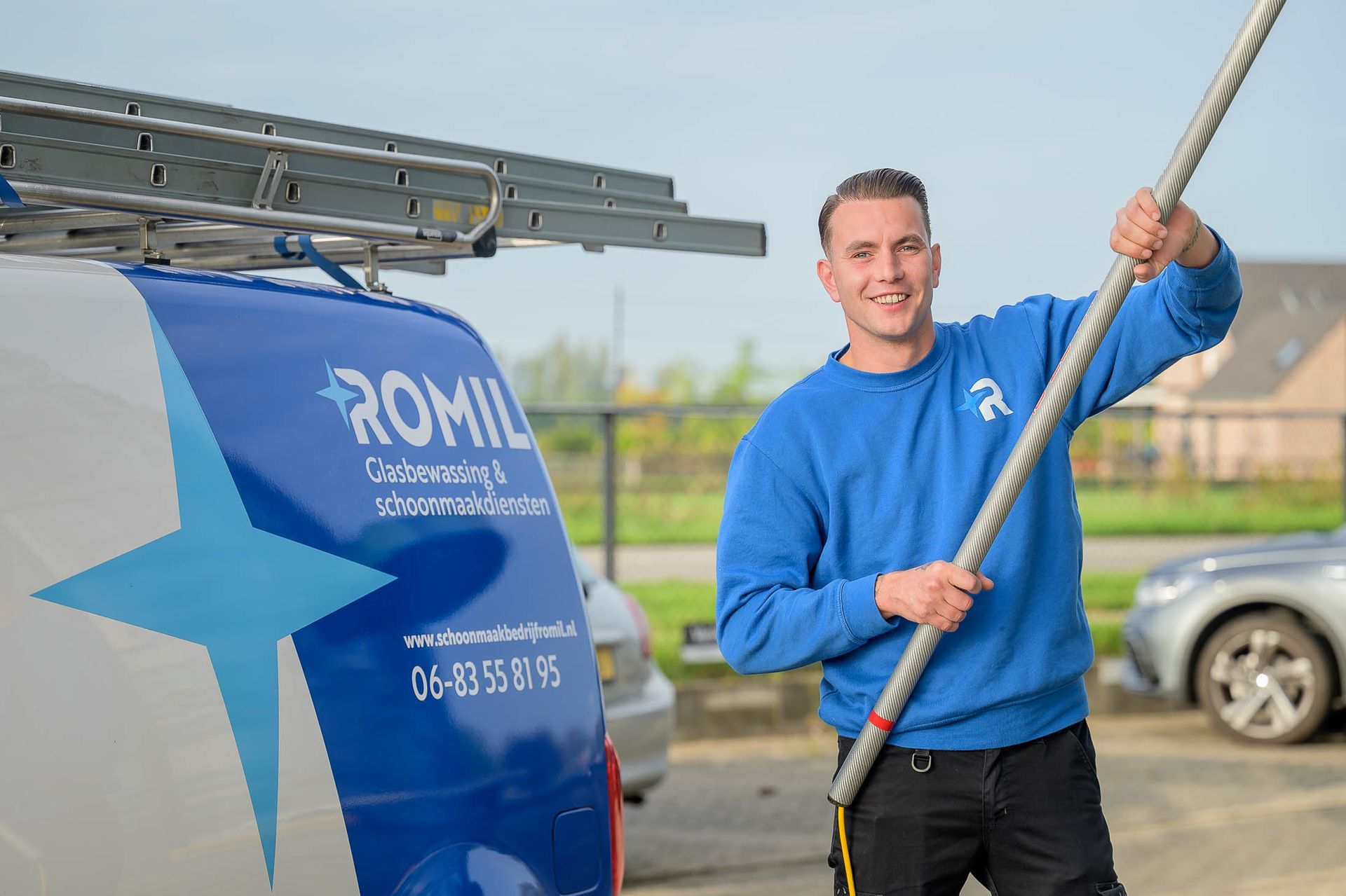 Een man in een blauwe trui houdt een stok vast voor een busje.