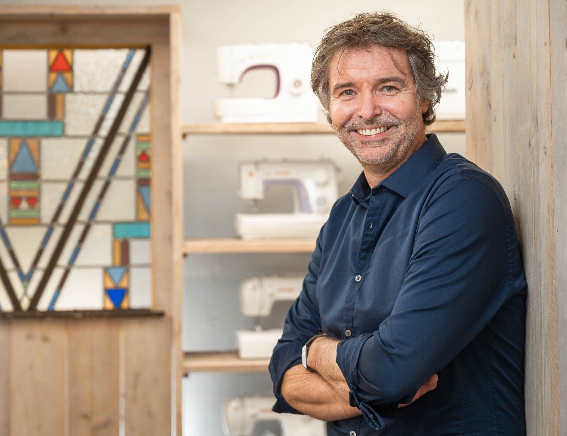 Een man leunt tegen een muur, met zijn armen over elkaar en lacht.