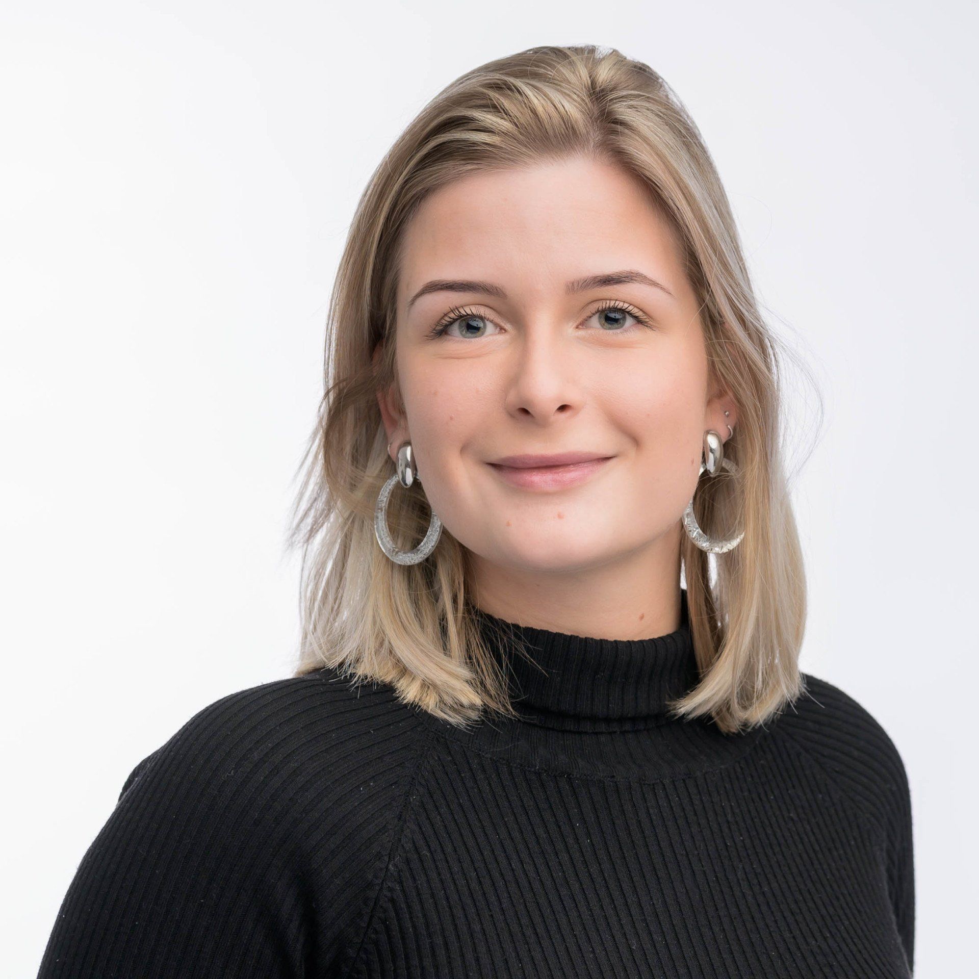 Een vrouw draagt een zwarte trui en hoepeloorbellen en lacht naar de camera.