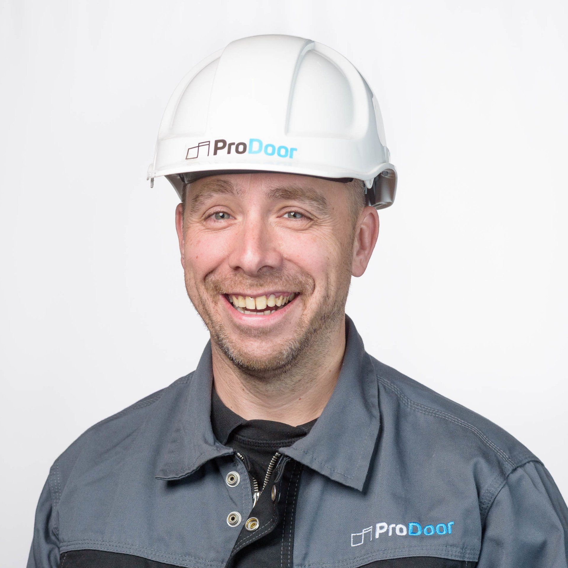 Een man met een helm en een overall lacht.