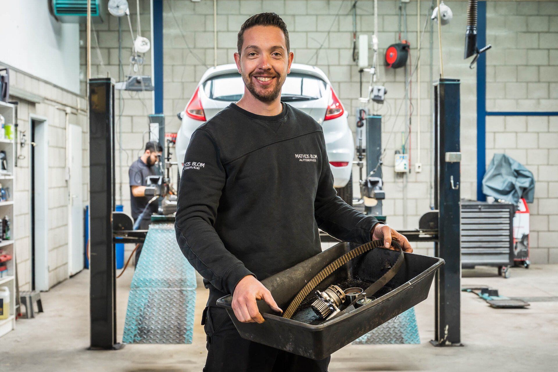 Een man houdt een bak met gereedschap vast in een garage.