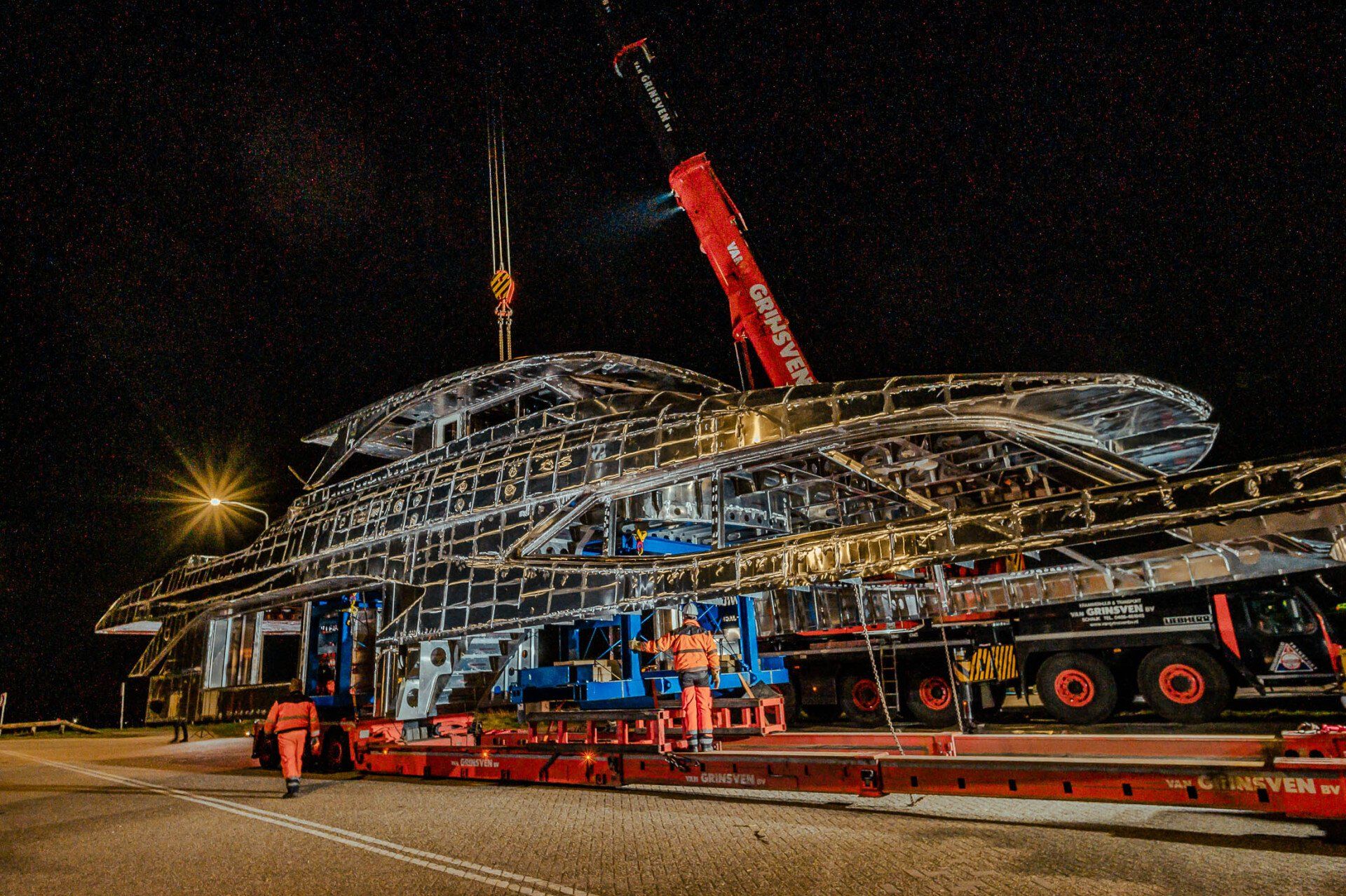 's Nachts wordt een groot schip door een kraan opgetild.
