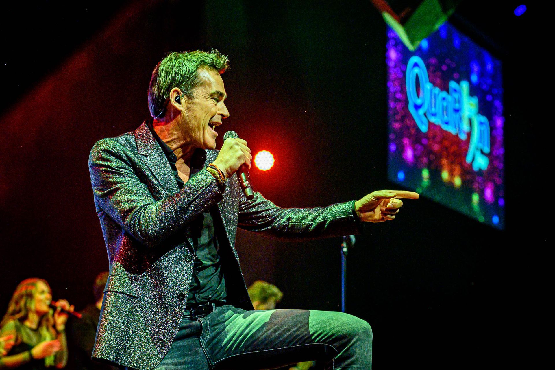Een man in pak zingt in een microfoon op een podium.