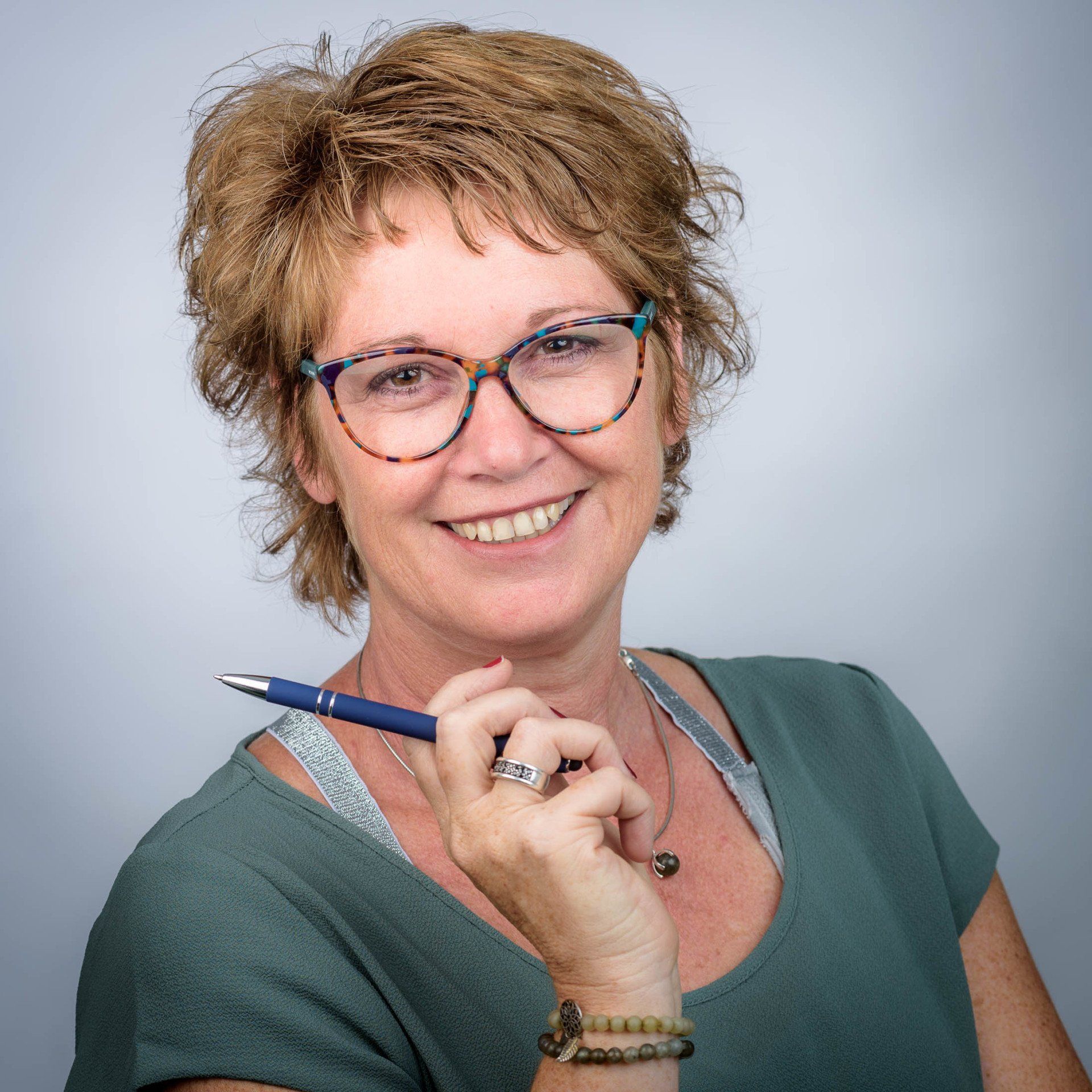 Een vrouw met een bril lacht en houdt een pen vast