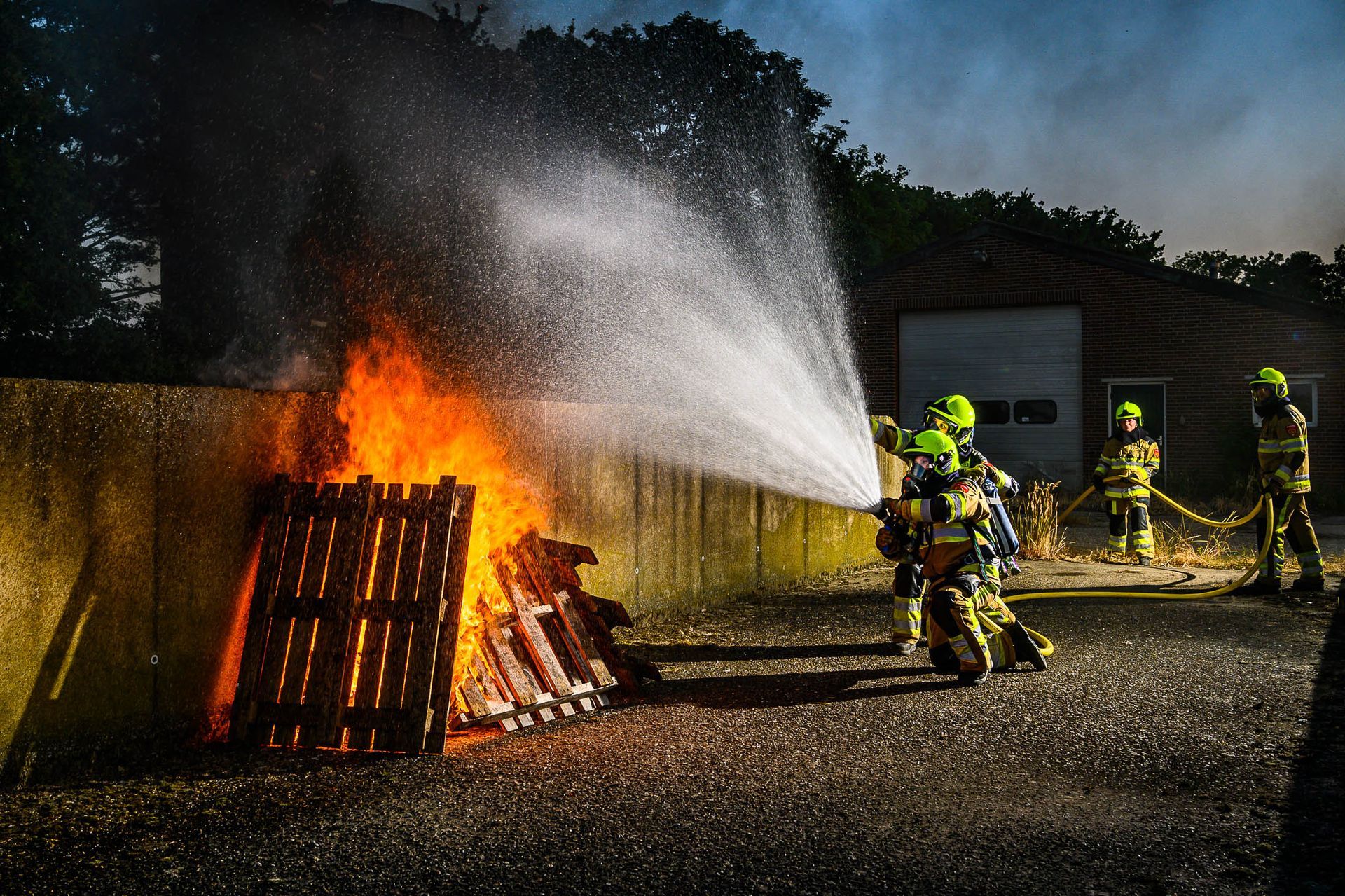 Een groep brandweerlieden spuit water op een brand.