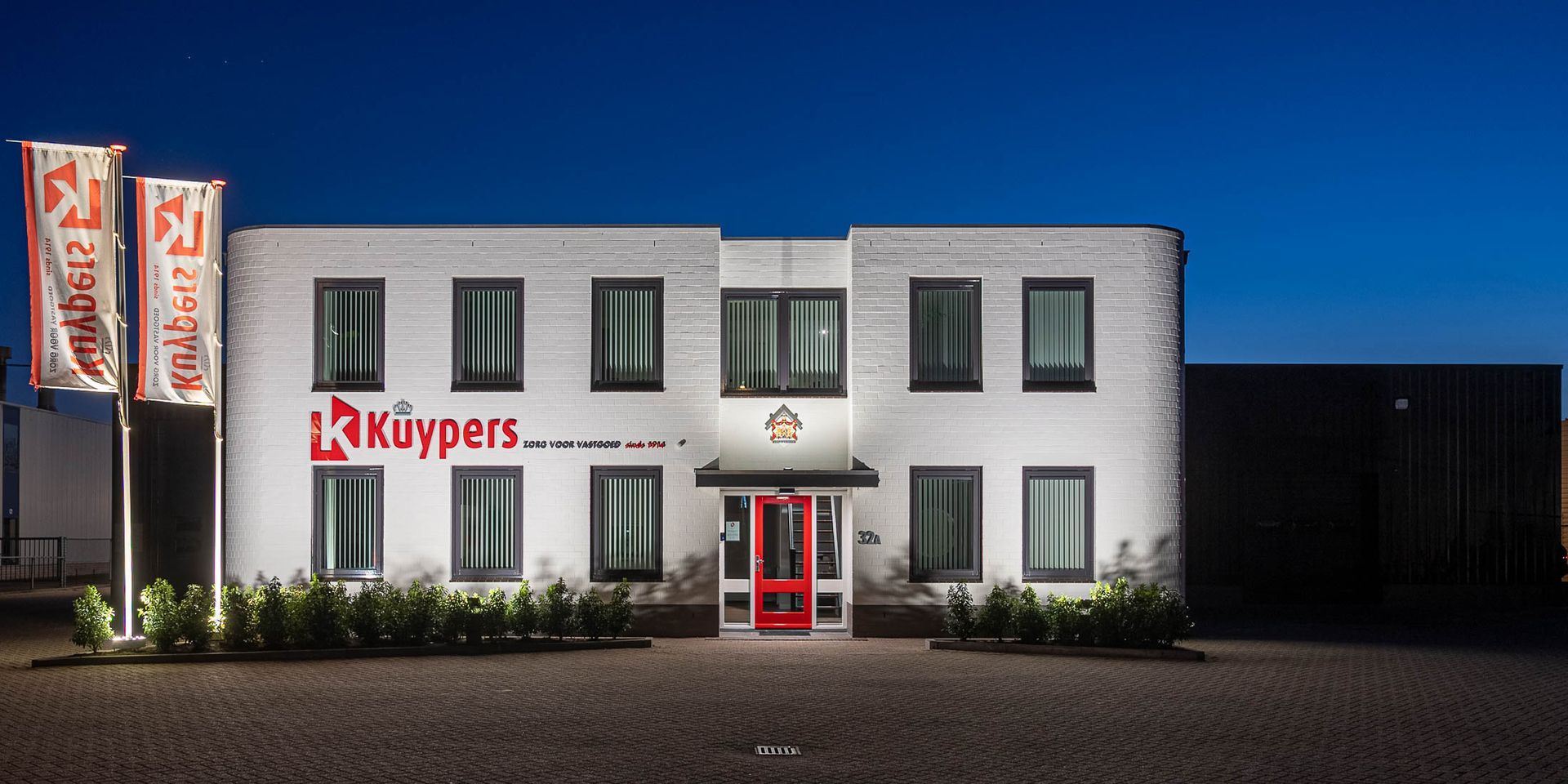 Een groot wit gebouw met een rode deur is 's nachts verlicht.