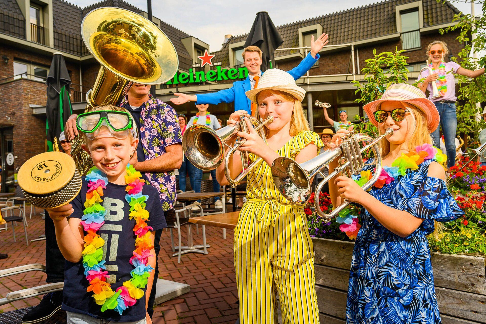 Een groep kinderen bespeelt een muziekinstrument voor een Heineken-bord.