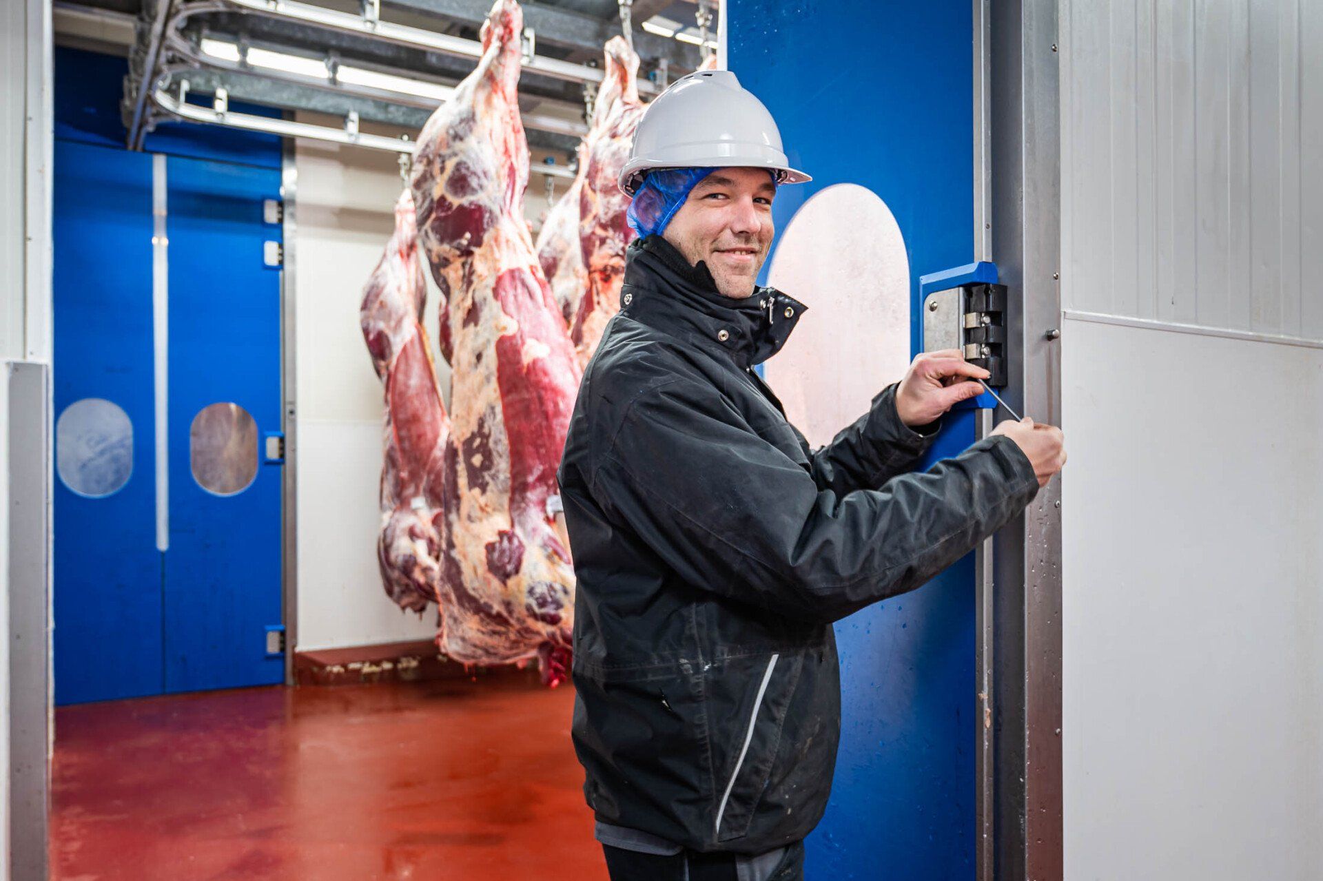 Een man met een helm opent een deur in een vleesfabriek.