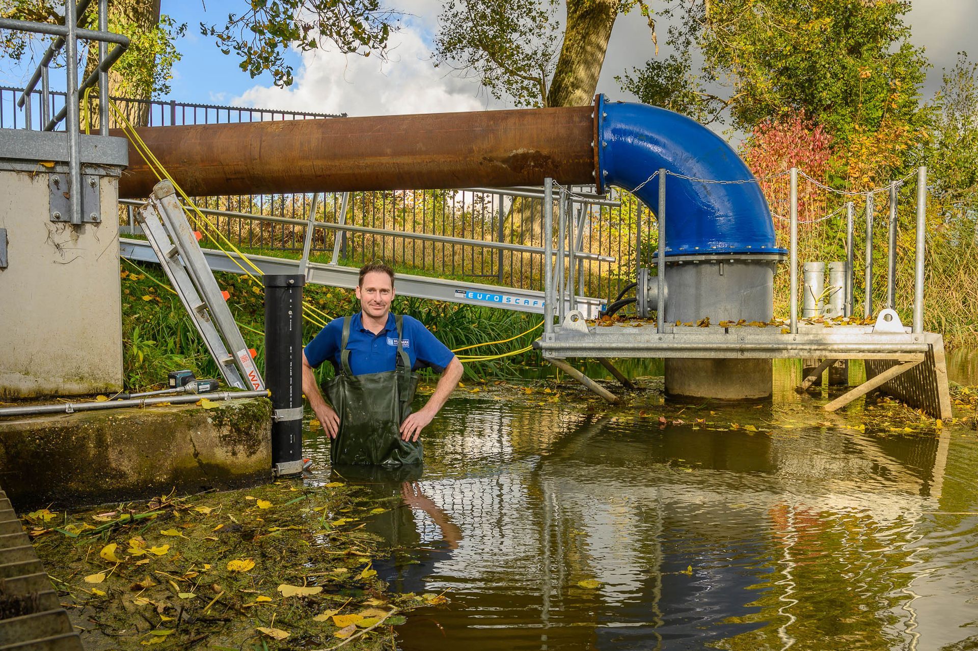 Een man staat in het water bij een pijp.