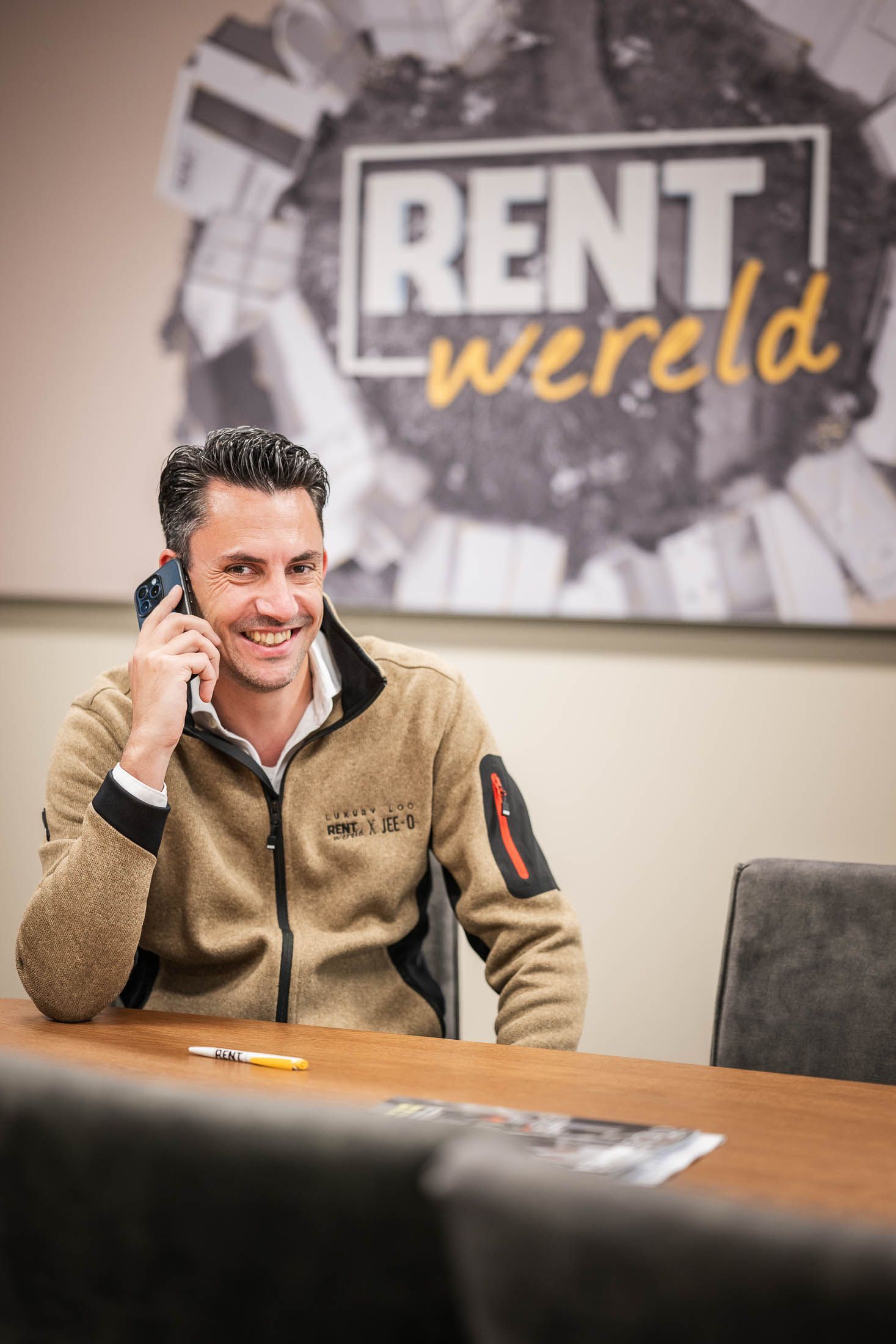Een man zit aan een tafel en belt via een mobiele telefoon.
