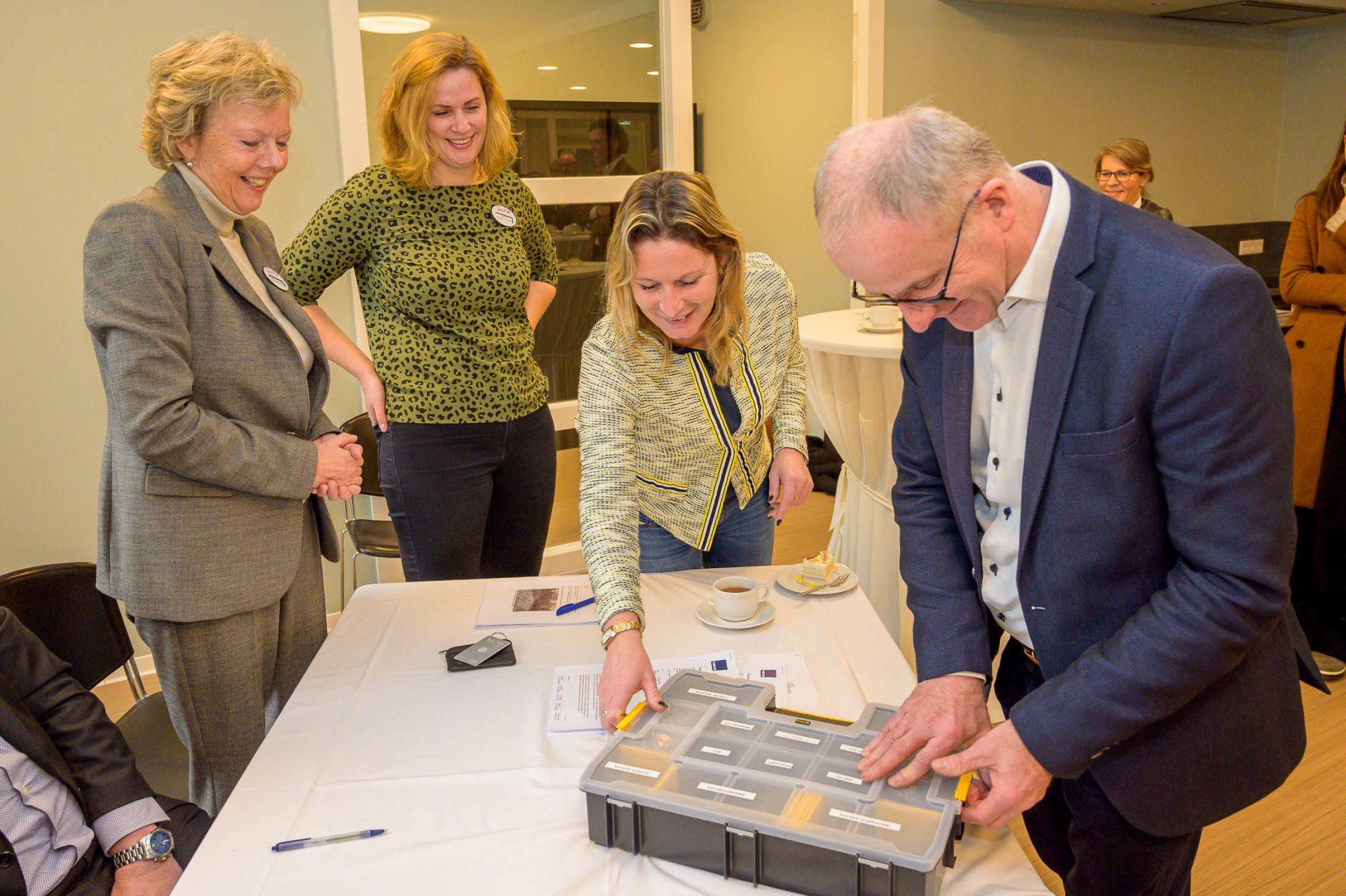 Een groep mensen staat rond een tafel en kijkt naar een doos.