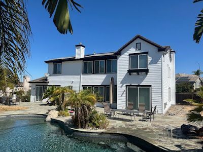 White house with pool, palm trees, and outdoor seating on a sunny day.