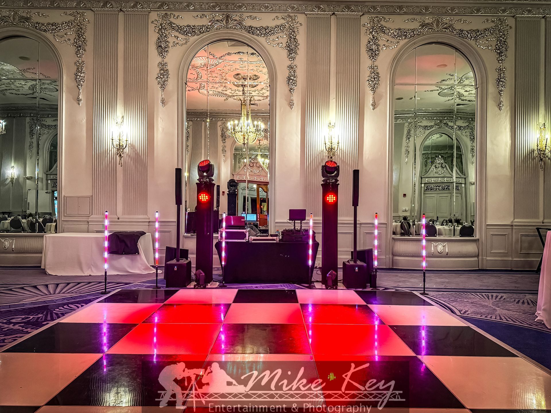 A formal ballroom setup with a black and white checkerboard dance floor, DJ equipment, and vertical light bars.