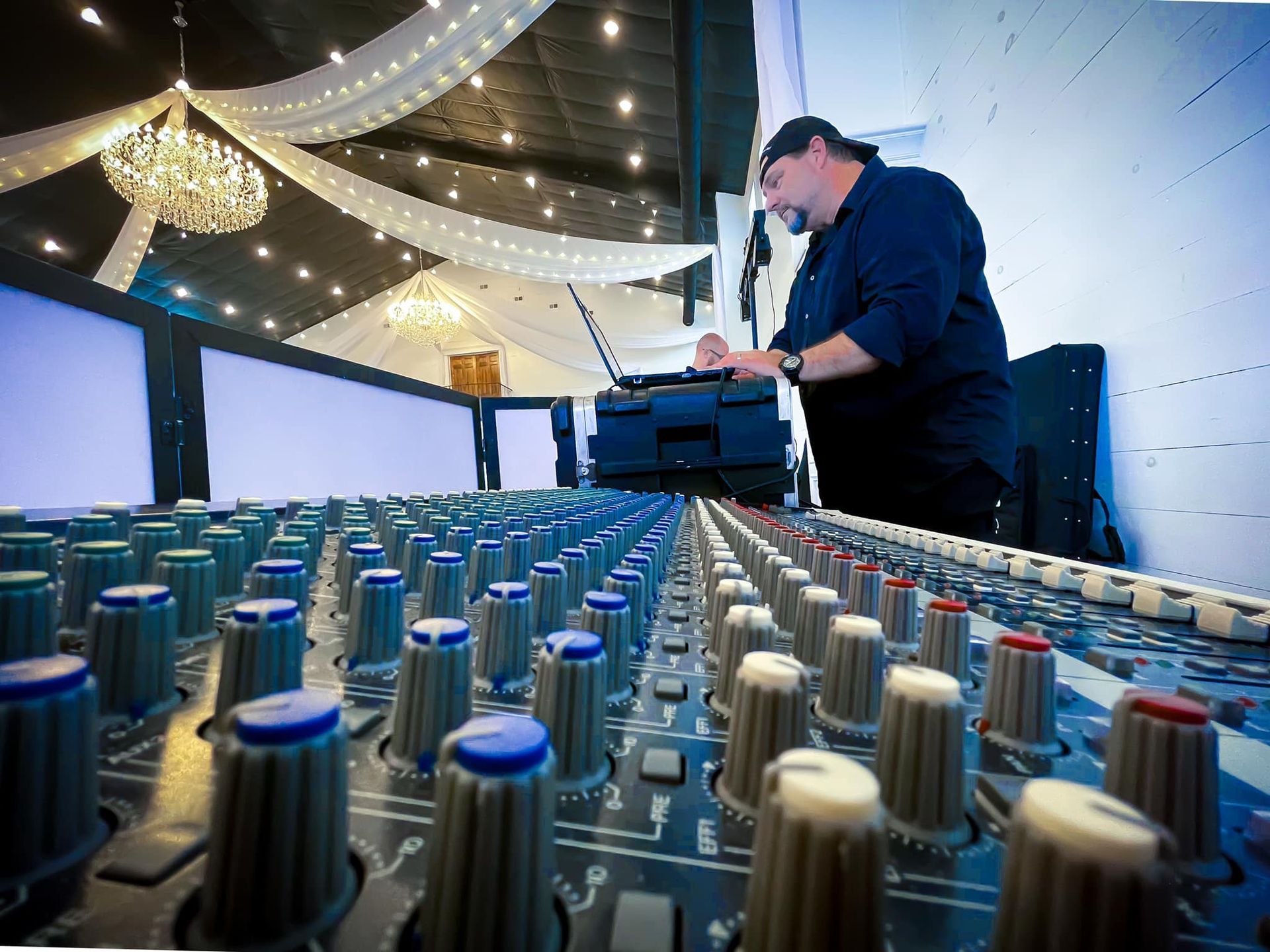 A person stands at a large audio mixing console in a decorated event hall, adjusting equipment controls.