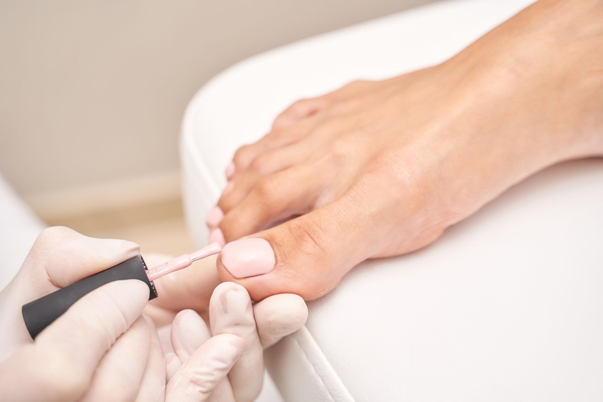 Manicure in progress as gloved hands paint a toenail with pale pink polish